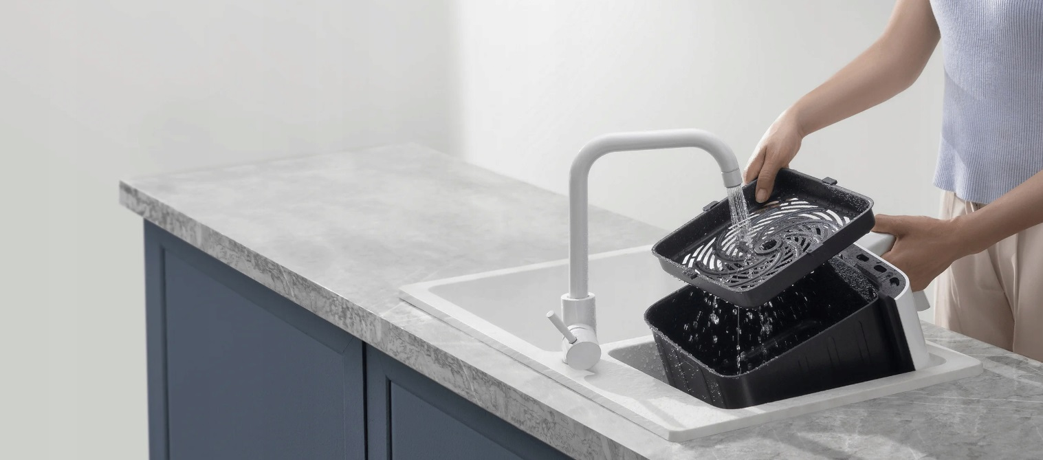 Osoba myjąca części frytownicy w zlewie. Części są czarne, a zlew biały.