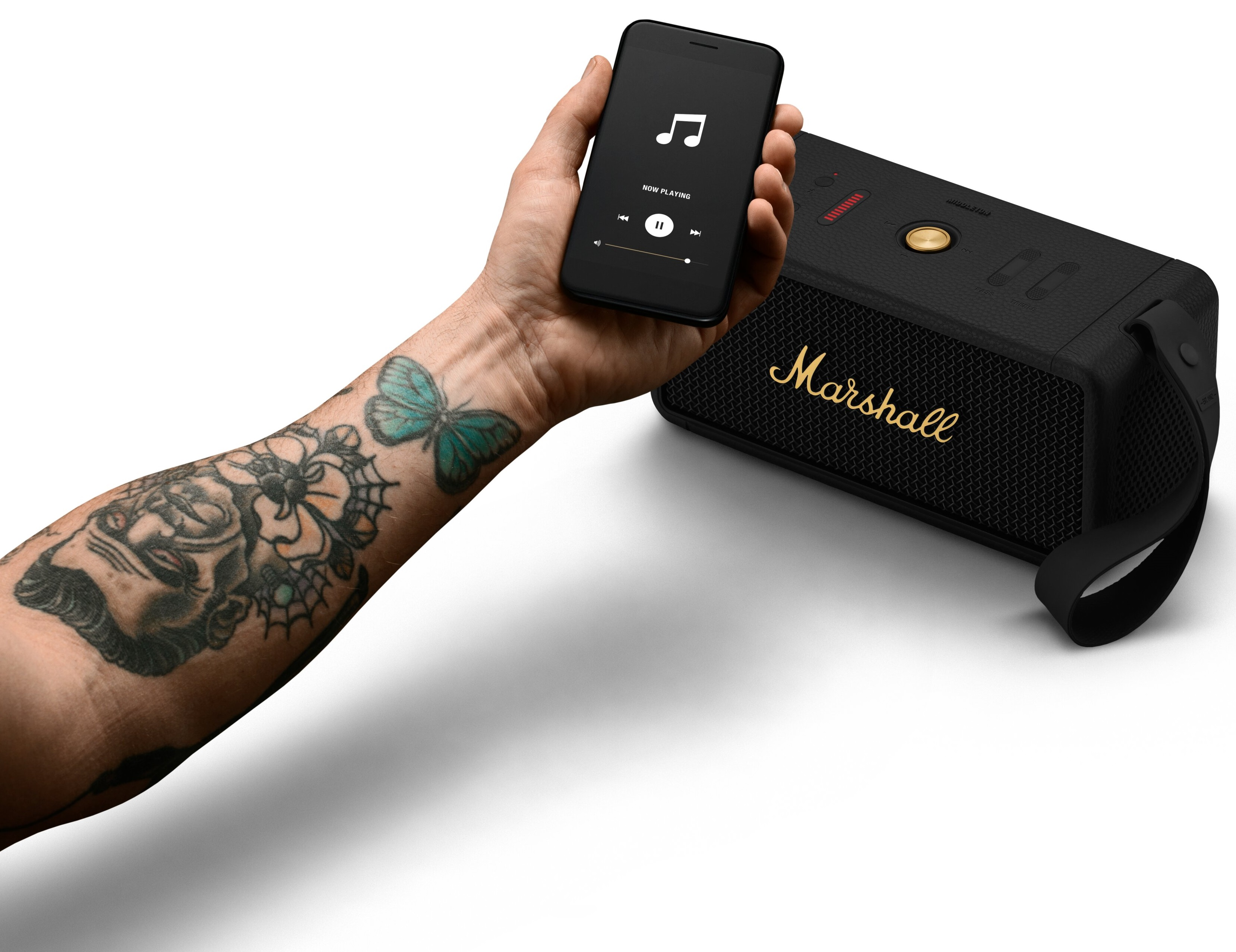 Ręka osoby trzyma czarny telefon odtwarzający muzykę obok czarnego głośnika Marshall.