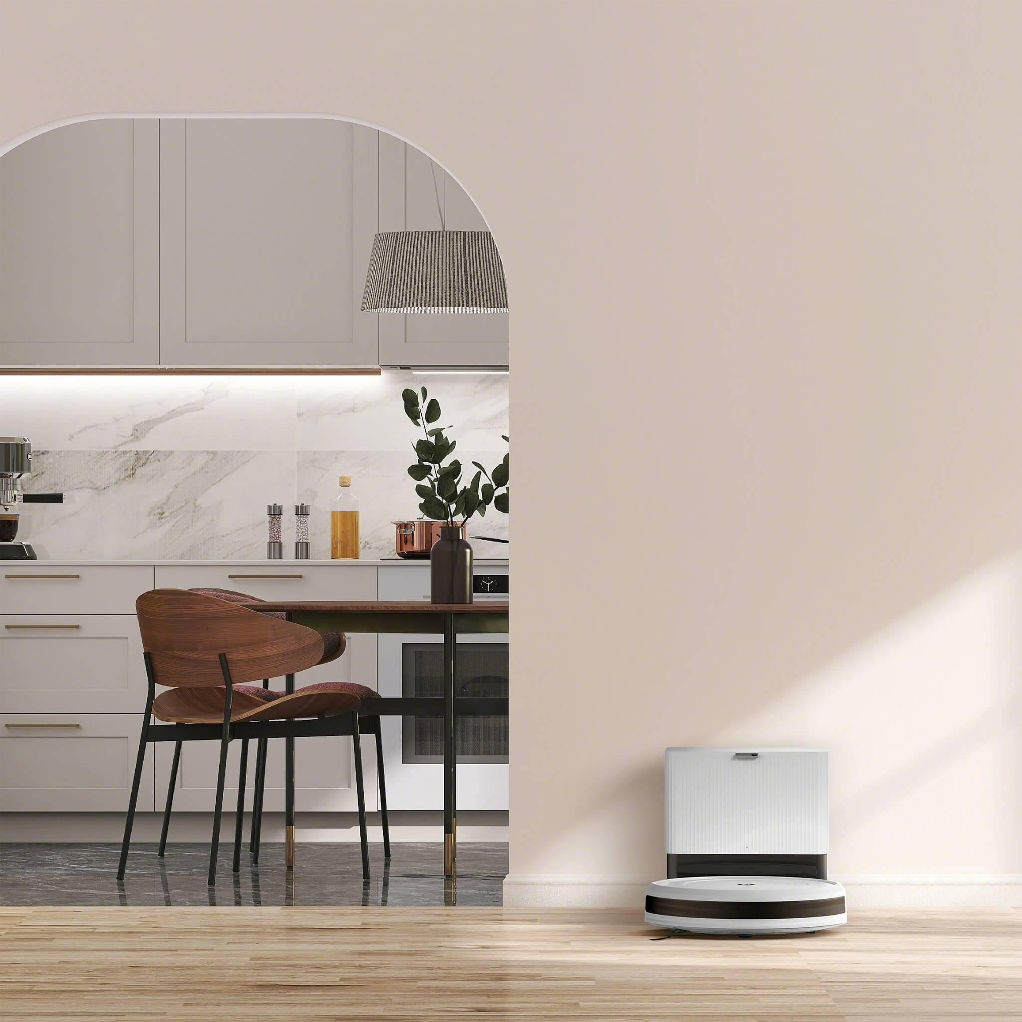 Nowoczesna kuchnia z robotem sprzątającym na pierwszym planie. Drewniana podłoga, białe ściany i szafki.