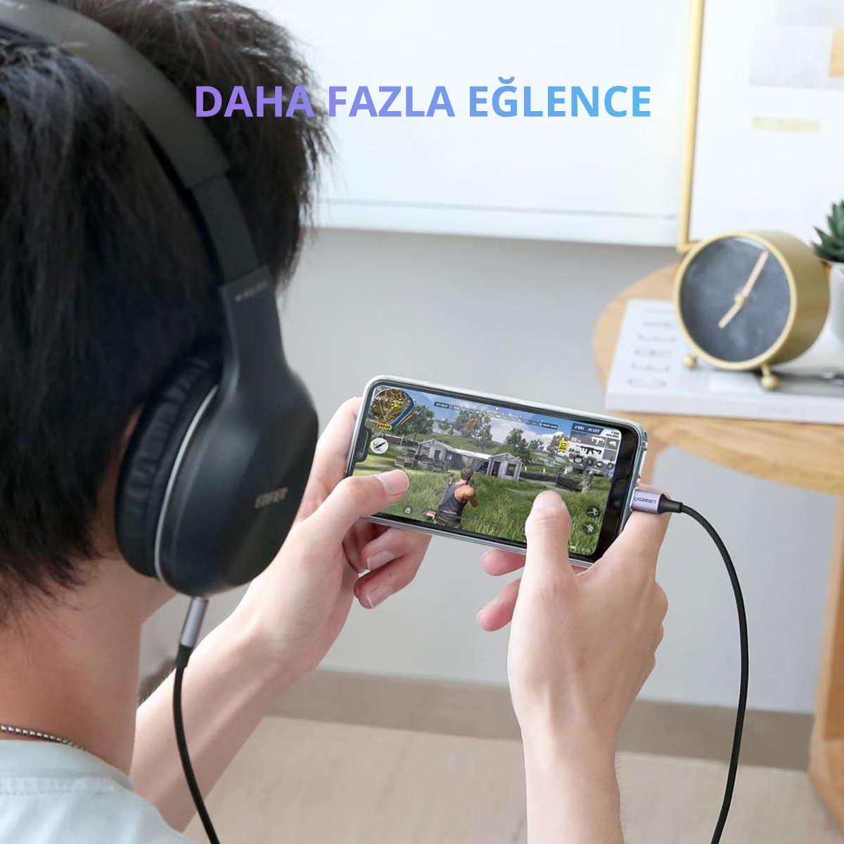 Kulaklık ve kablo bağlı, oyun oynayan birini gösteren telefon tutan bir kişi.