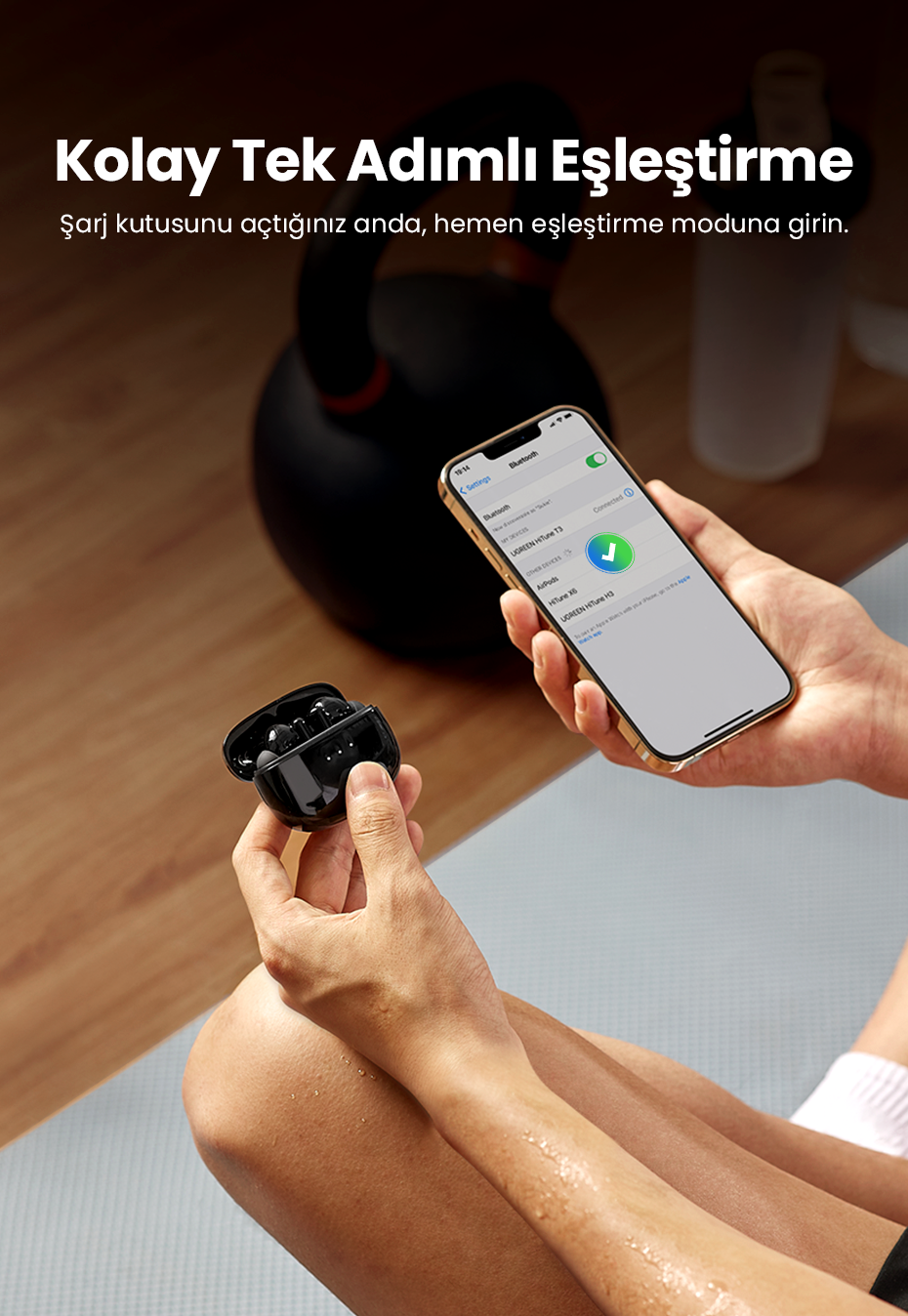 Kişi, siyah kulaklık kutusu ve bağlı bir Bluetooth cihazı gösteren bir telefon tutuyor.