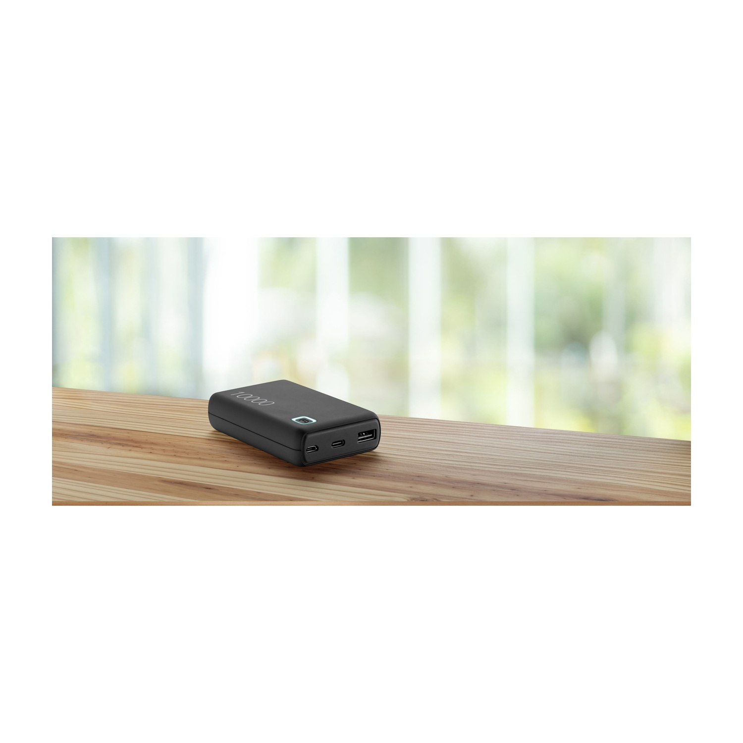 Power bank nero su un tavolo di legno con una finestra sfocata sullo sfondo.