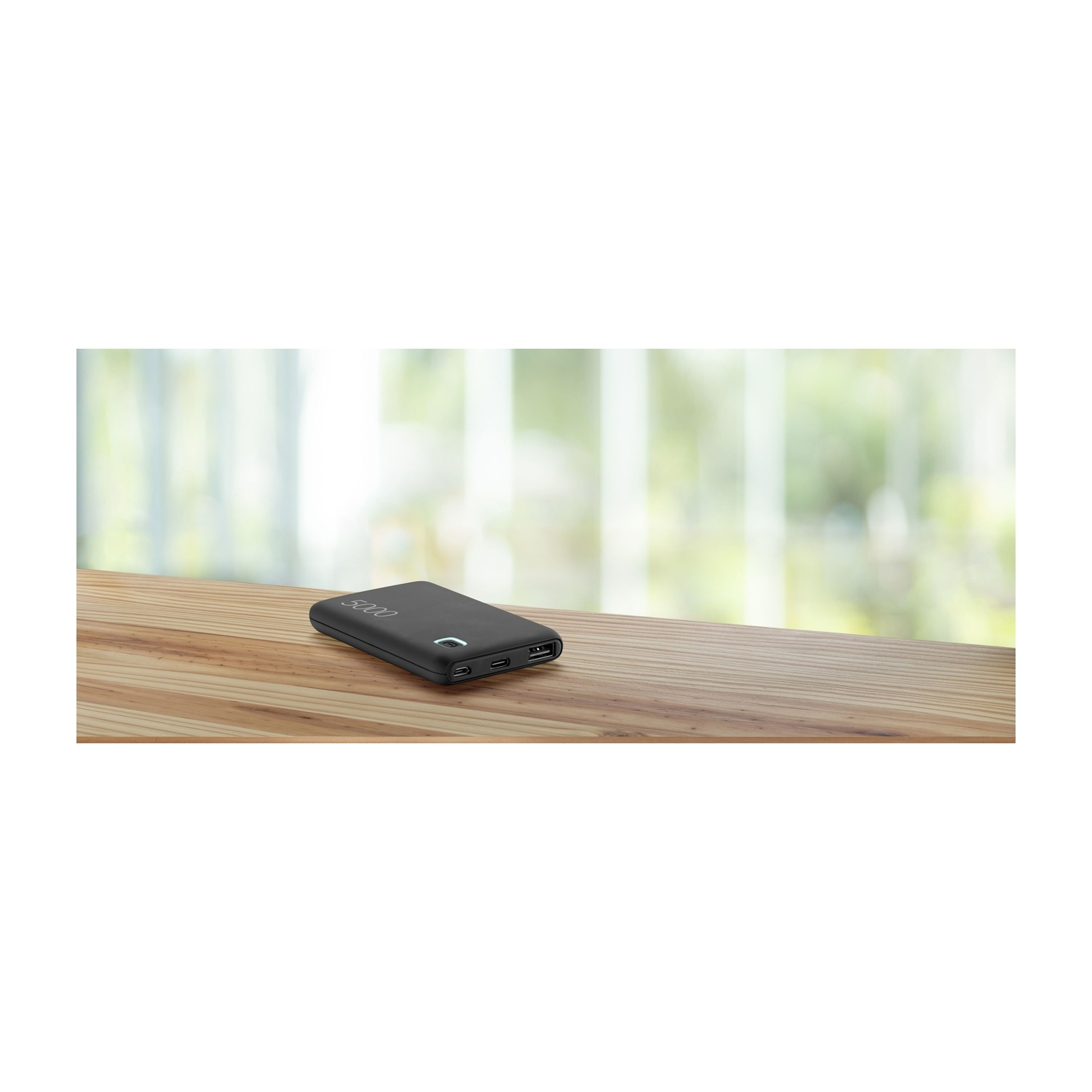 Power bank nero su un tavolo di legno. Una finestra sfocata sullo sfondo.