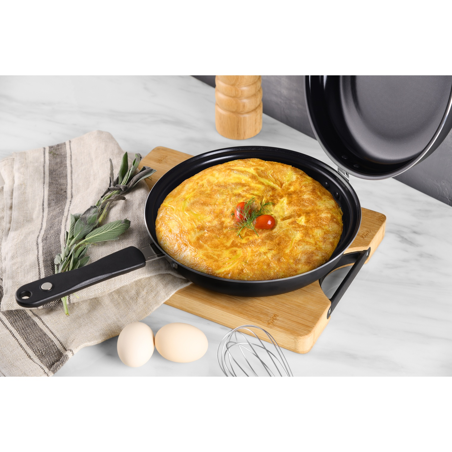 Padella con frittata, su tagliere con uova, frusta ed erbe aromatiche.