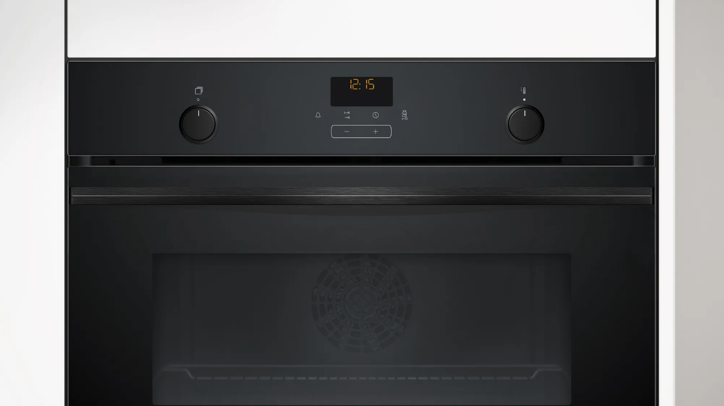 Un horno negro con una pantalla digital que muestra la hora. Perillas a cada lado. Fondo blanco.