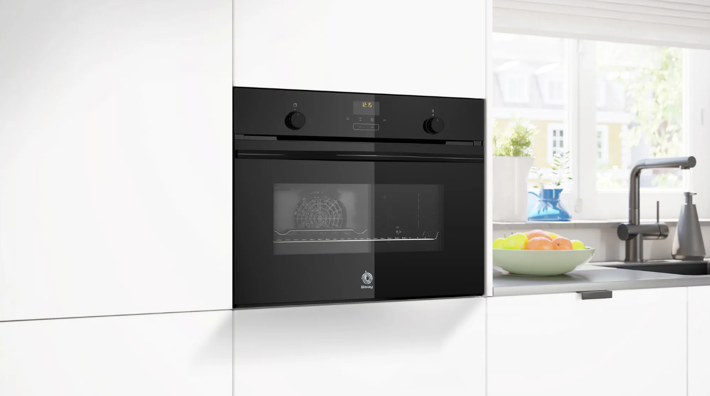 Horno empotrado negro en una cocina blanca. Una ventana está en el fondo.