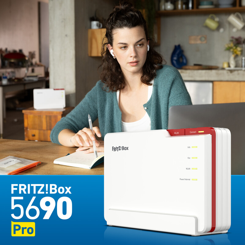 Frau sitzt an Holztisch mit Laptop, schreibt in Notizbuch, trägt Ohrhörer. FRITZ!Box Router auf dem Tisch.