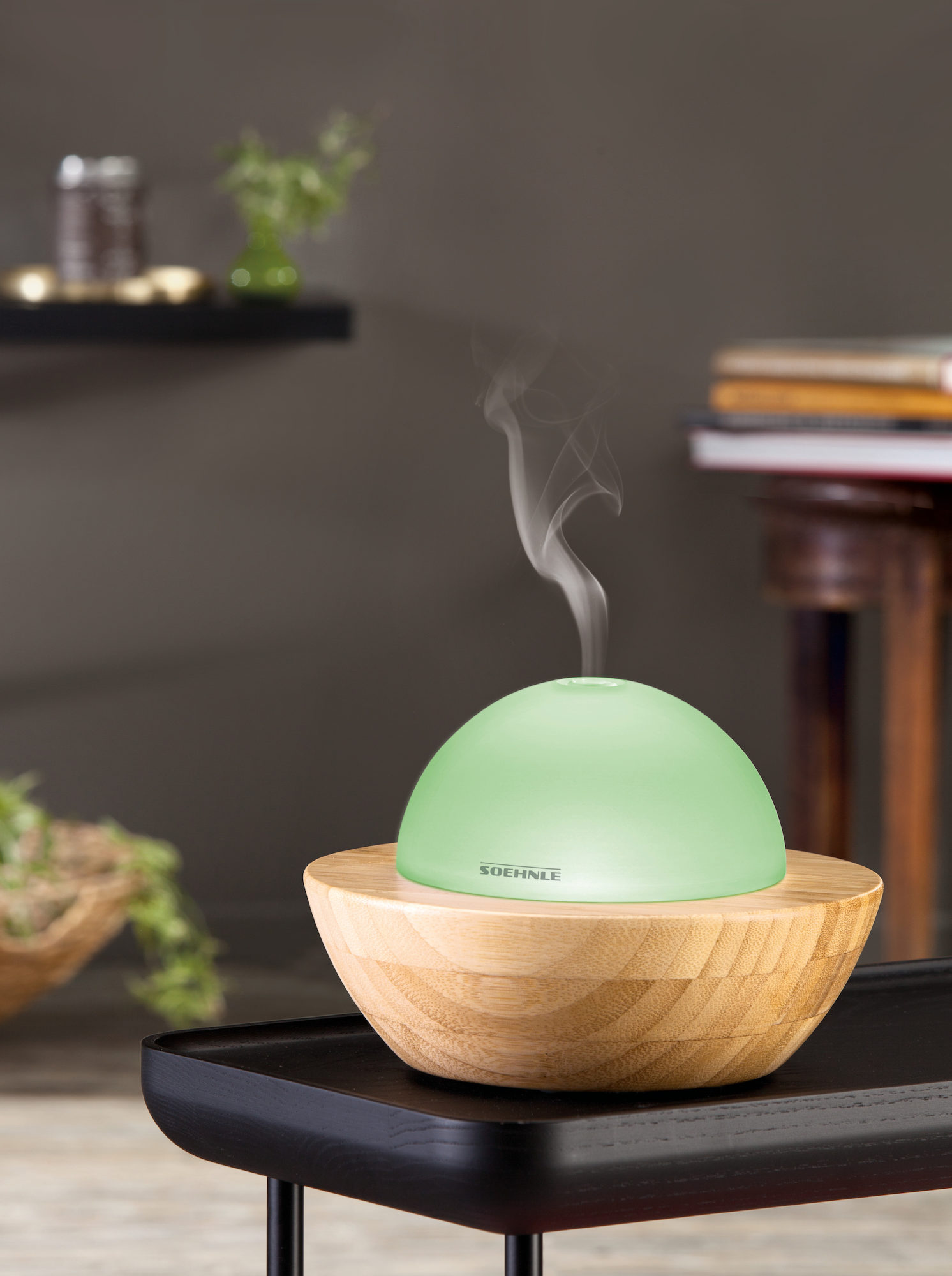 Zielony nawilżacz na drewnianej podstawie, emitujący parę, na stole.