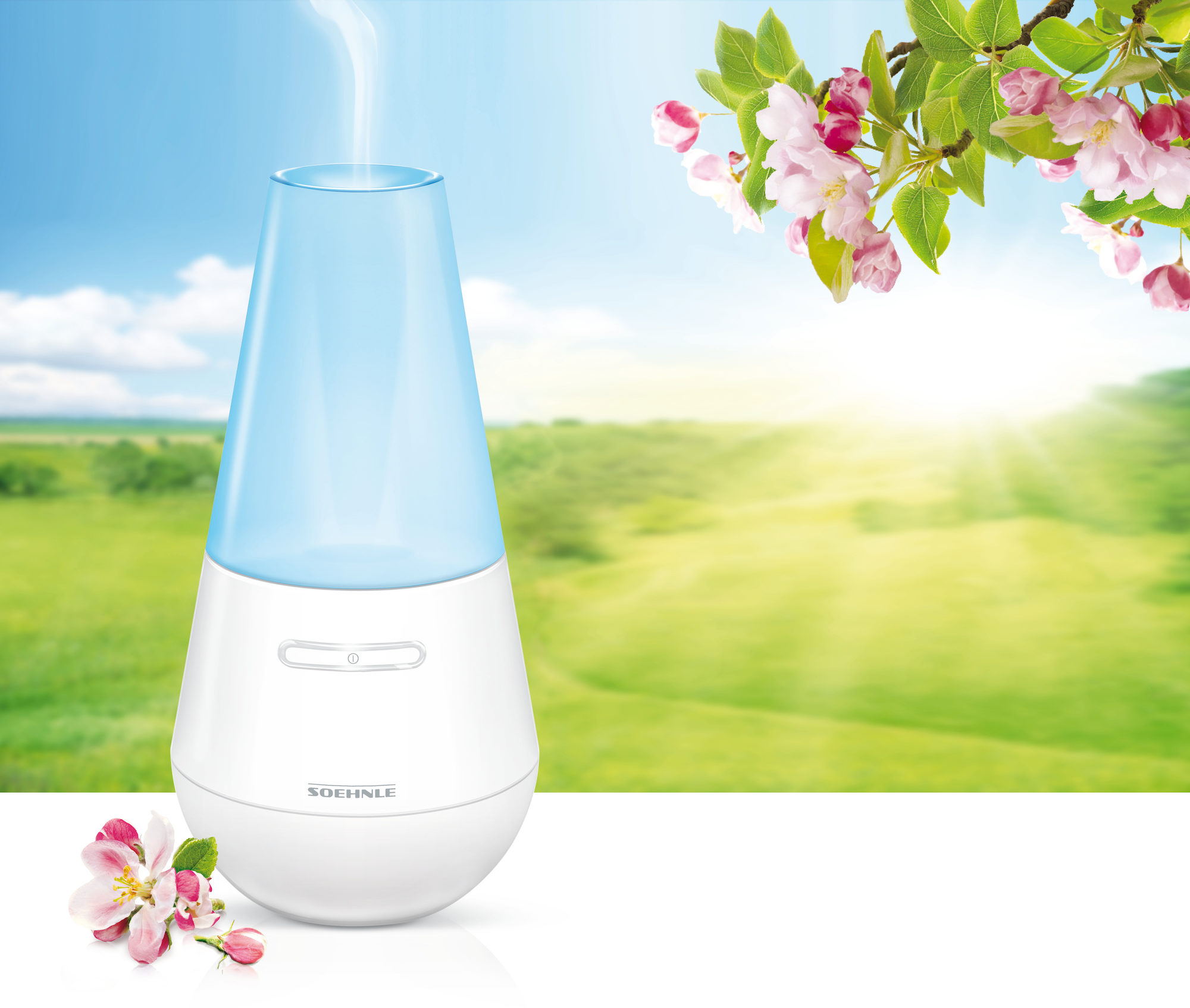 Biały nawilżacz z niebieskim wierzchem. Znajduje się na białej powierzchni, z zieloną trawą i różowymi kwiatami w tle.