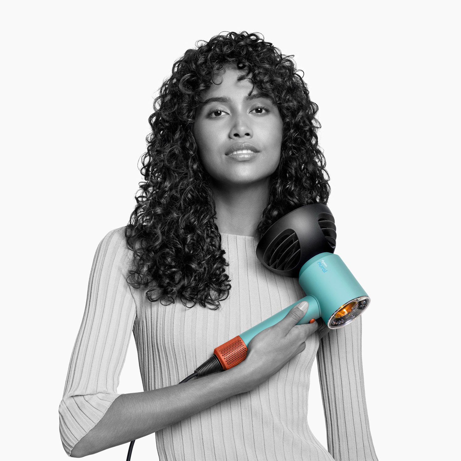 Kobieta z kręconymi włosami trzyma turkusowo-czarną suszarkę. Białe tło.