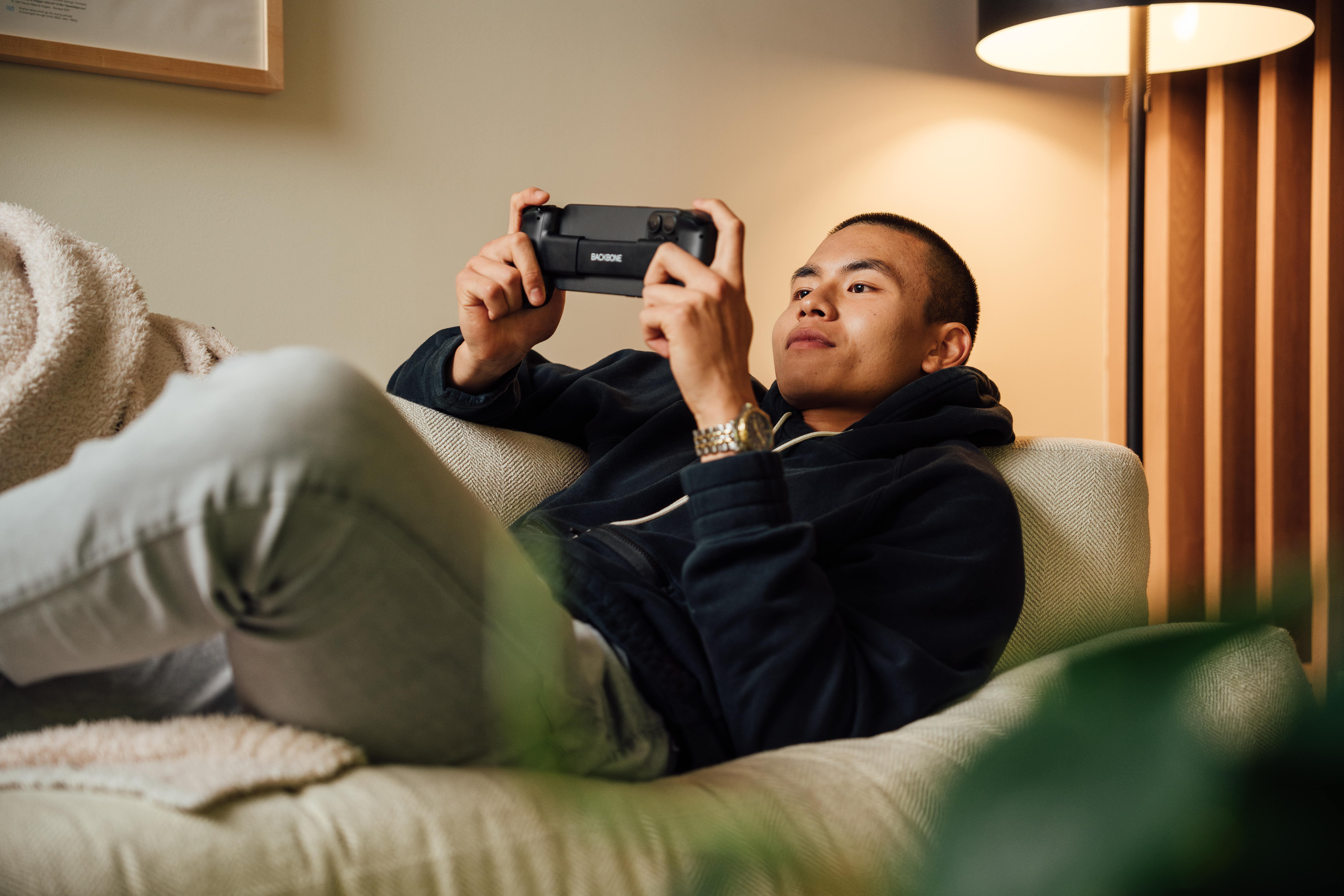 Mann liegt auf Couch und spielt Videospiel mit Controller.