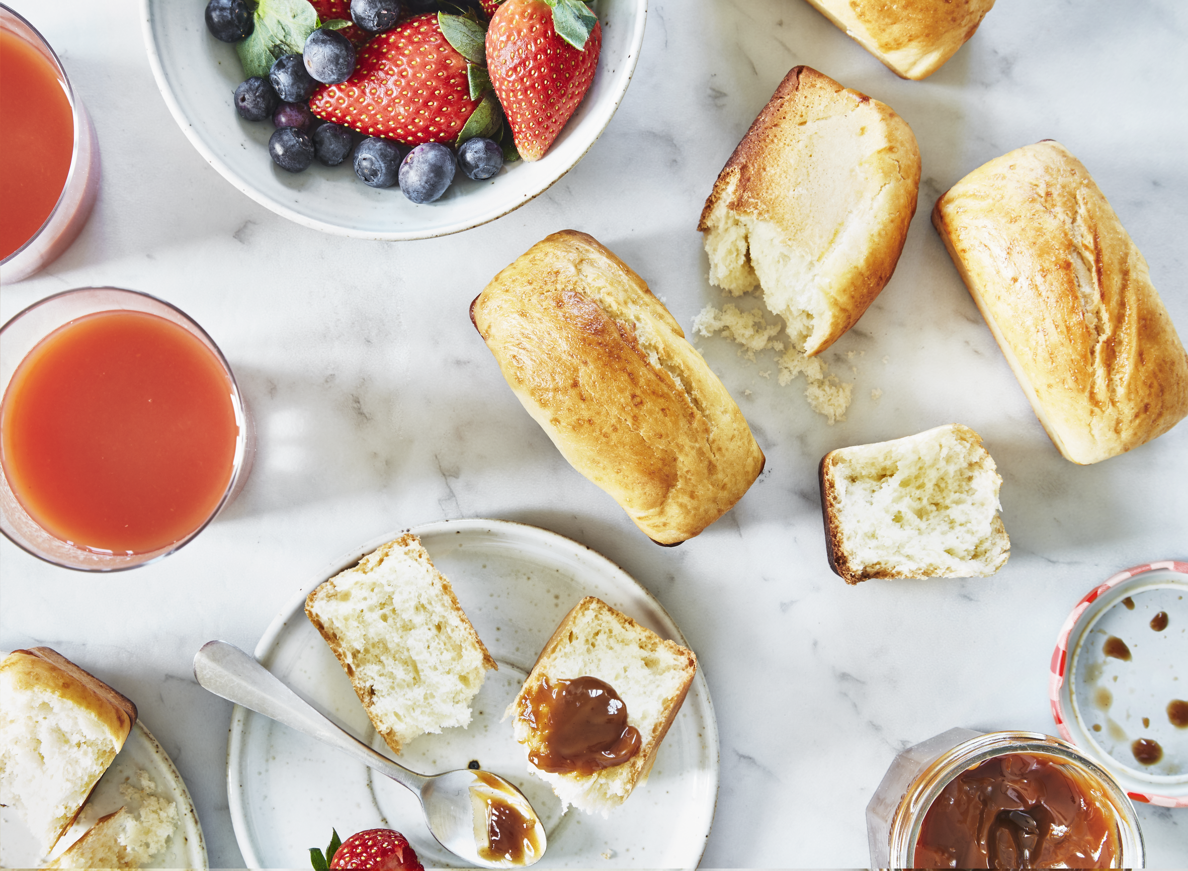 Widok z góry na jedzenie na marmurowej powierzchni. Zawiera bułki, dżem, jagody i sok.