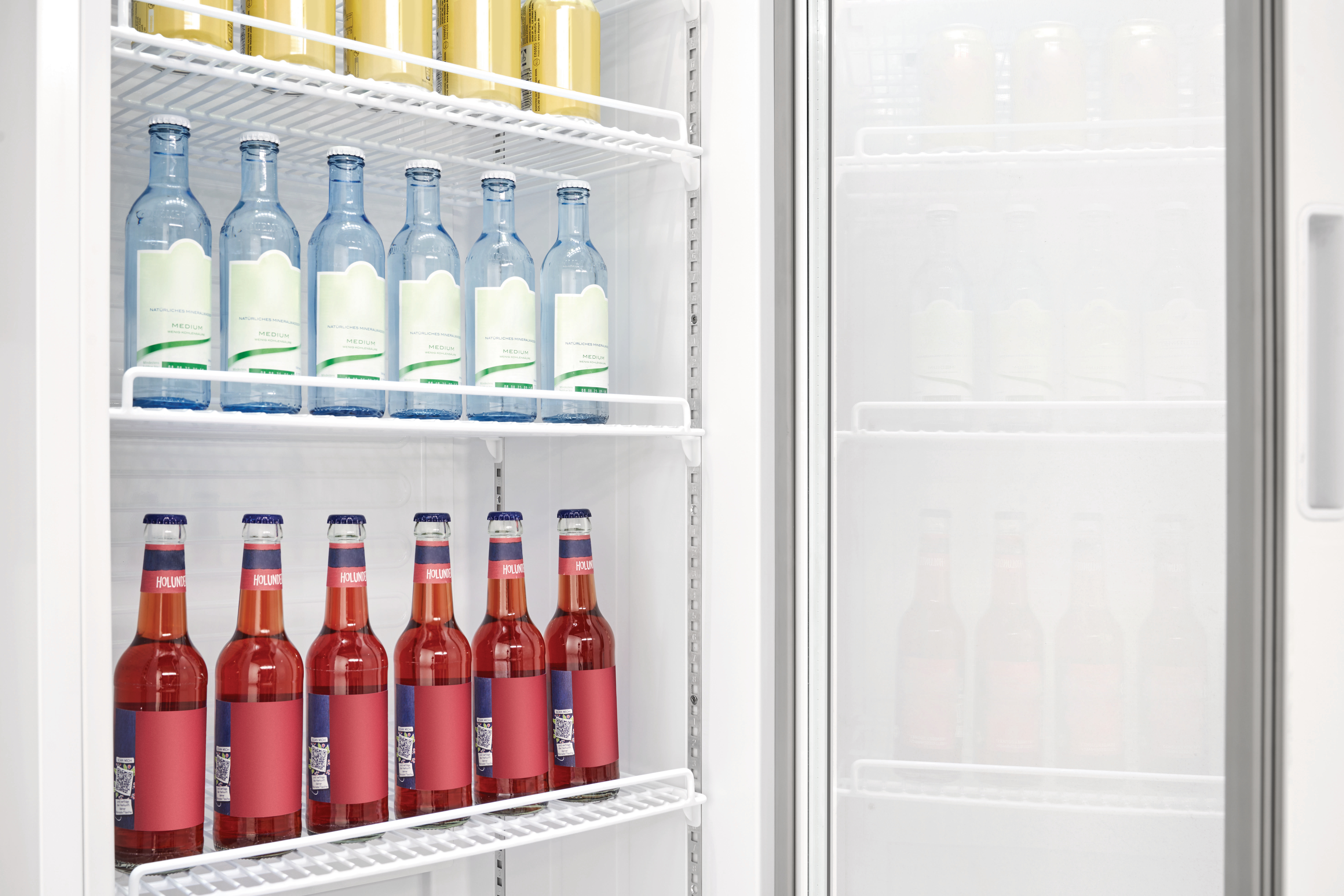 Ein Kühlschrank mit zwei Regalen zeigt Wasser- und Limonadenflaschen. Die Tür ist geöffnet und zeigt weitere Flaschen.