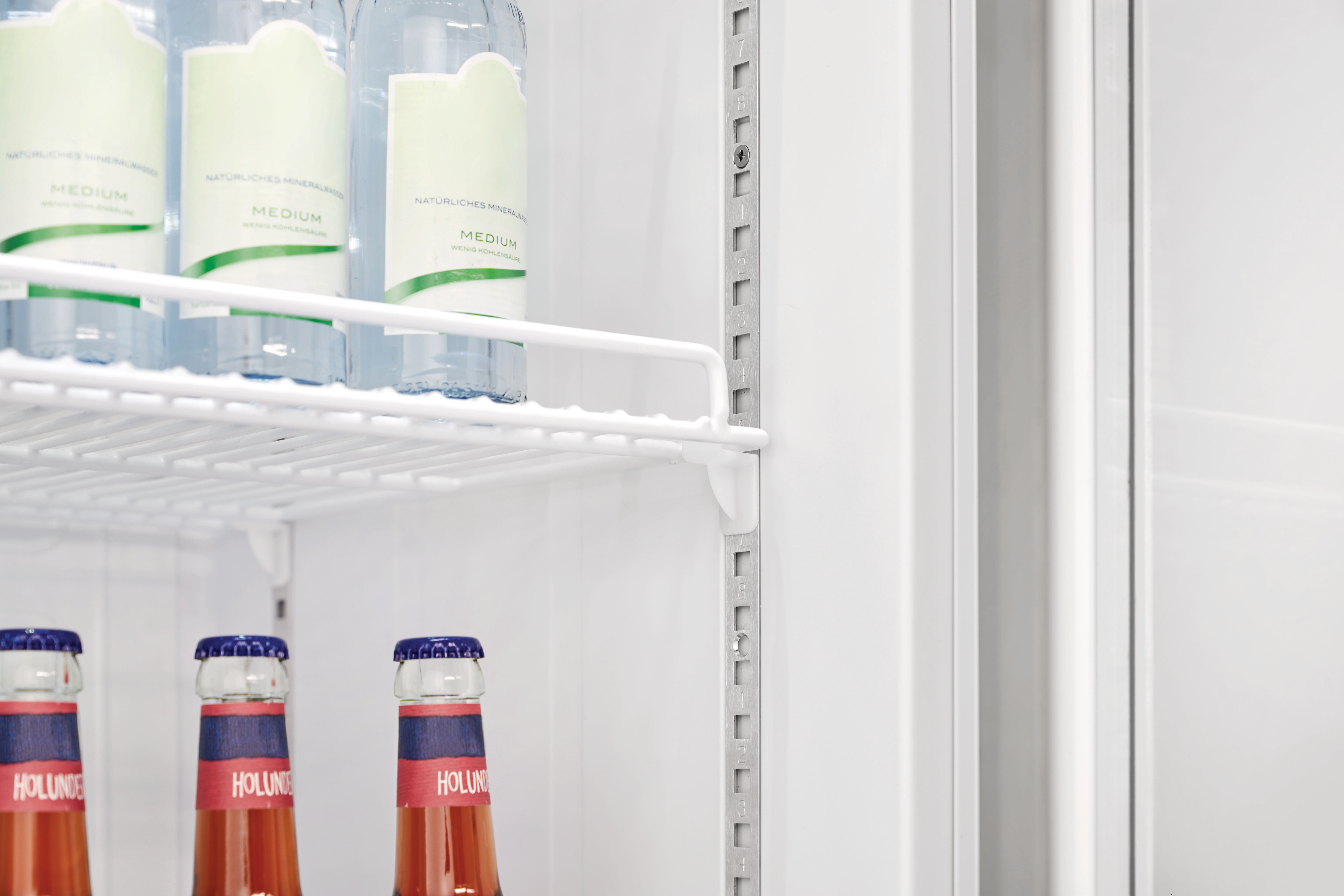 Im Kühlschrank: Wasserflaschen auf Regalen und darunter Sodaflaschen. Etiketten und Text sind sichtbar.