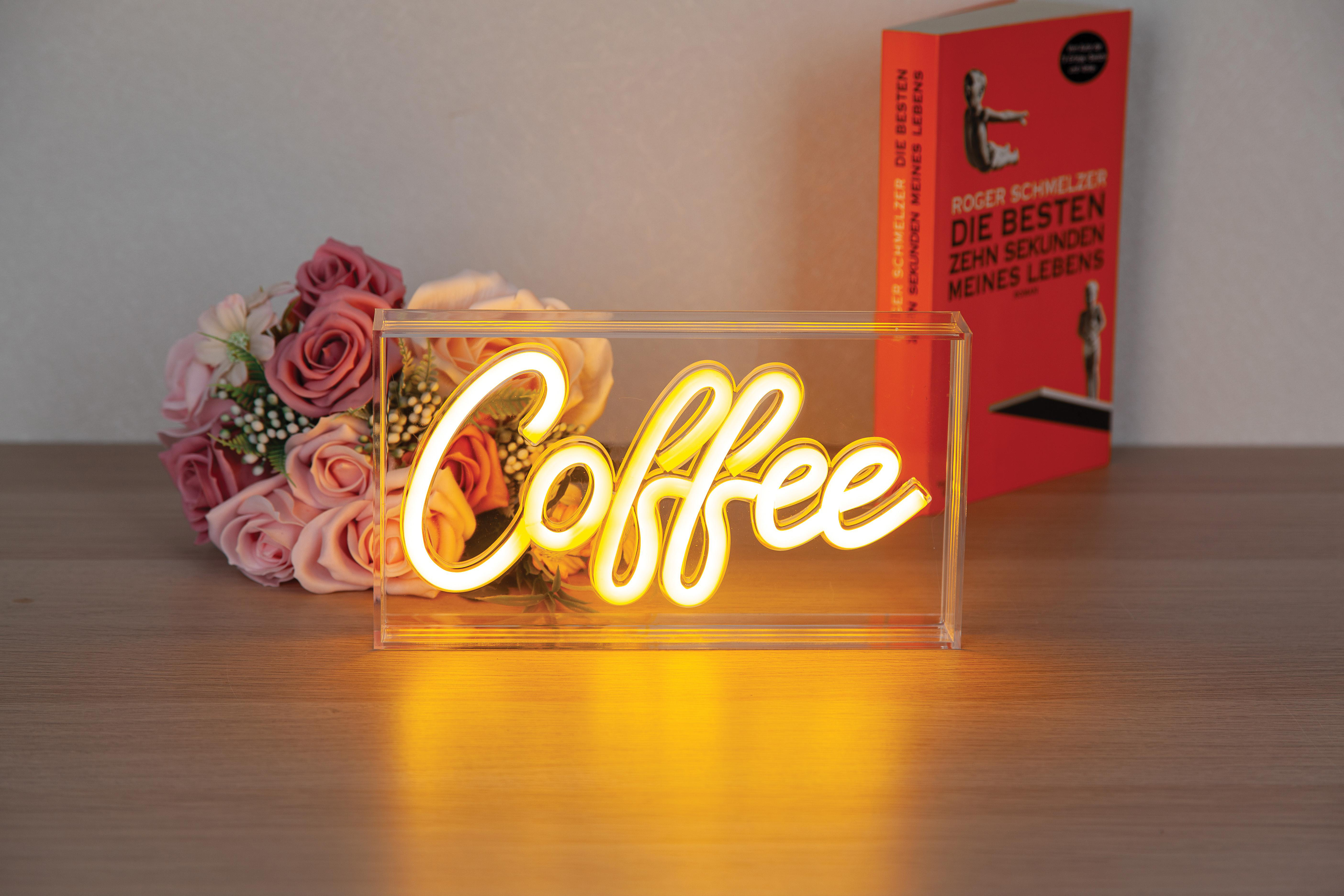 Ein Neon-„Coffee“-Schild in einer durchsichtigen Box, ein Blumenstrauß und ein Buch auf Holz.