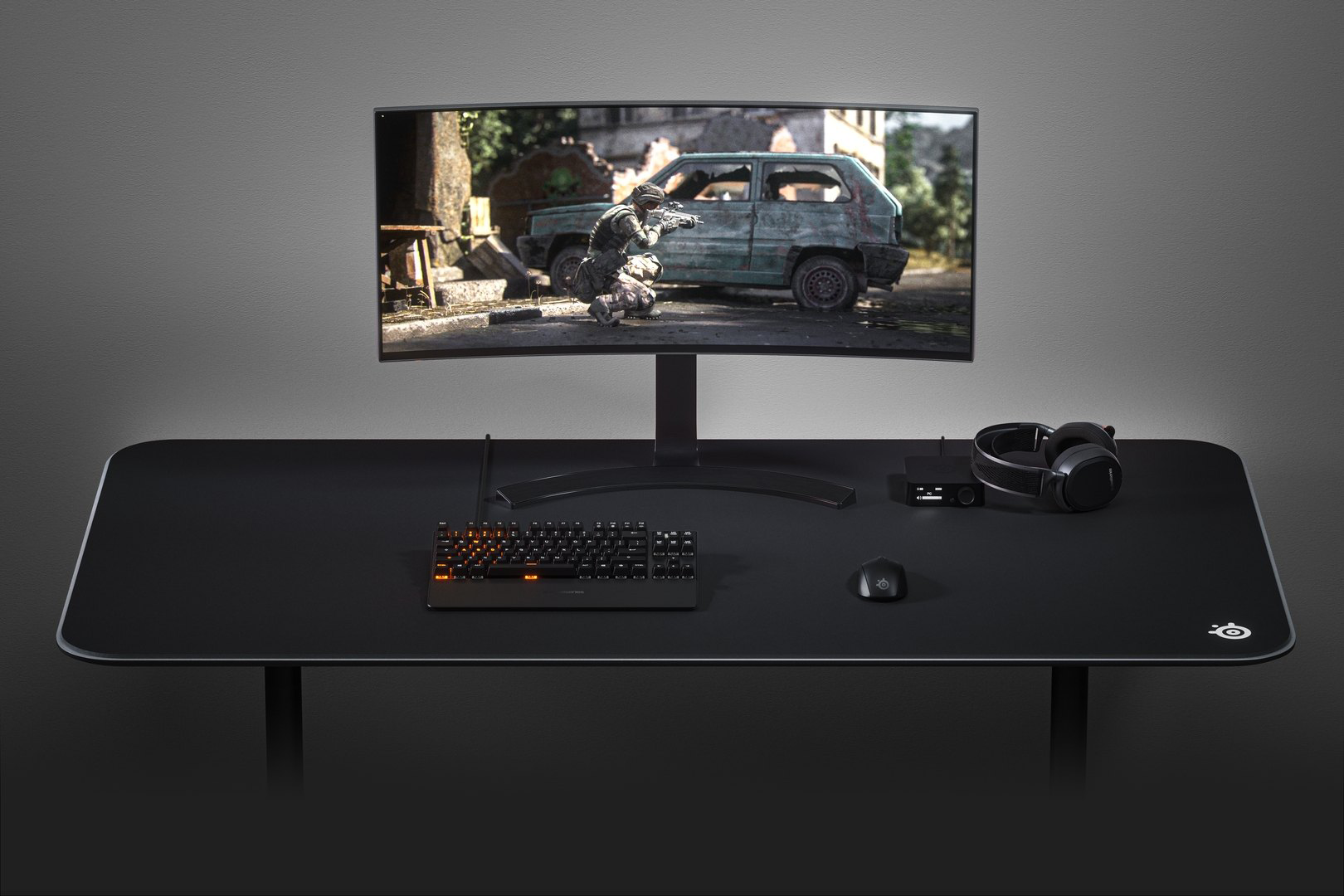 Gaming beállítás: ívelt monitor, billentyűzet, egér, fejhallgató fekete asztalon.