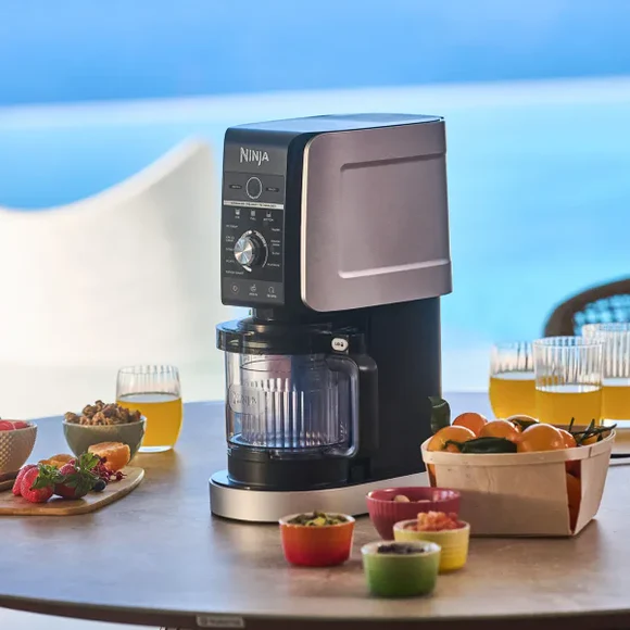 Ninja blender, malzemeler ve bardaklarla deniz kenarında bir masada.