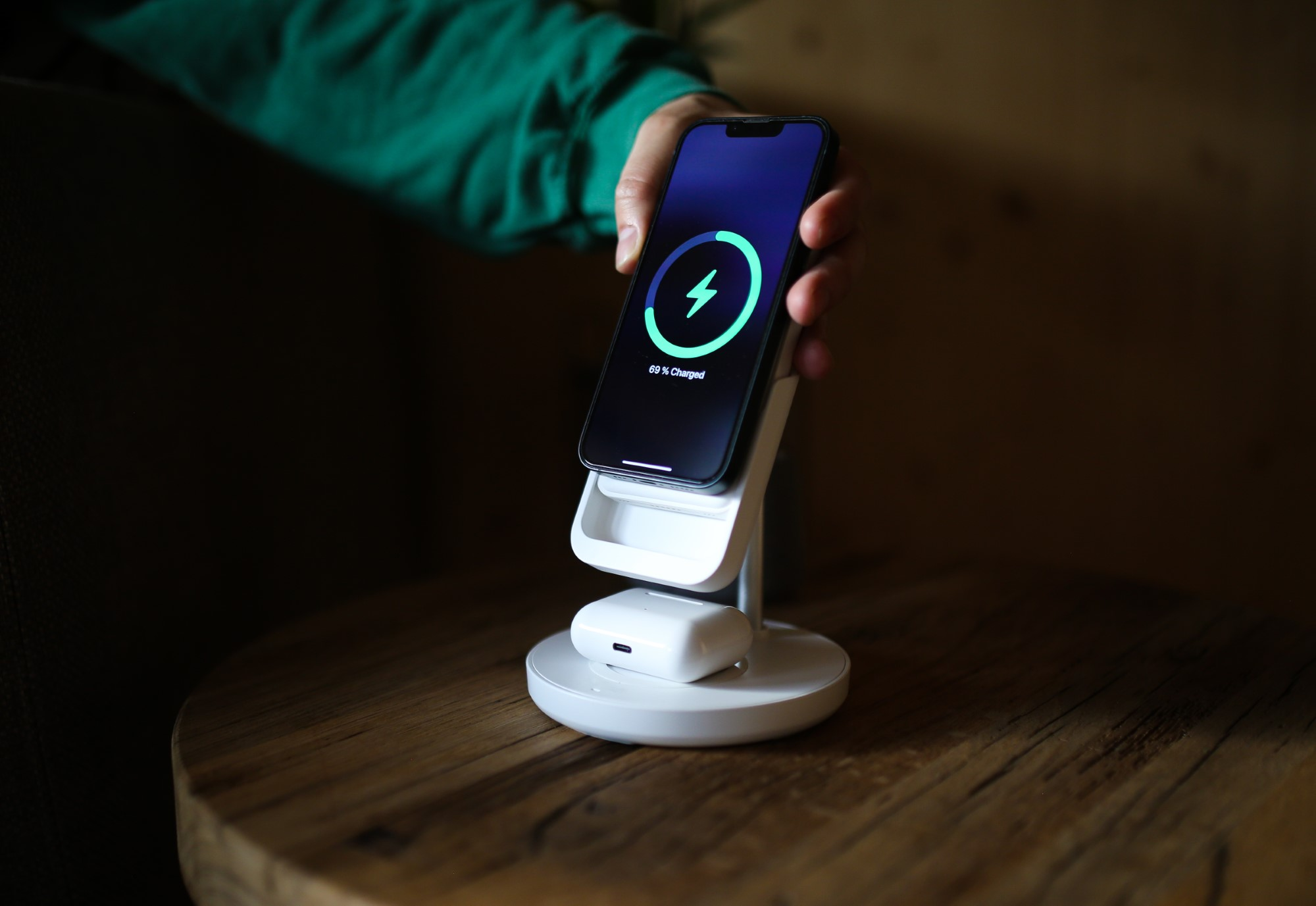 Ręka trzyma ładujący się telefon na białym stojaku. Ekran pokazuje błyskawicę.