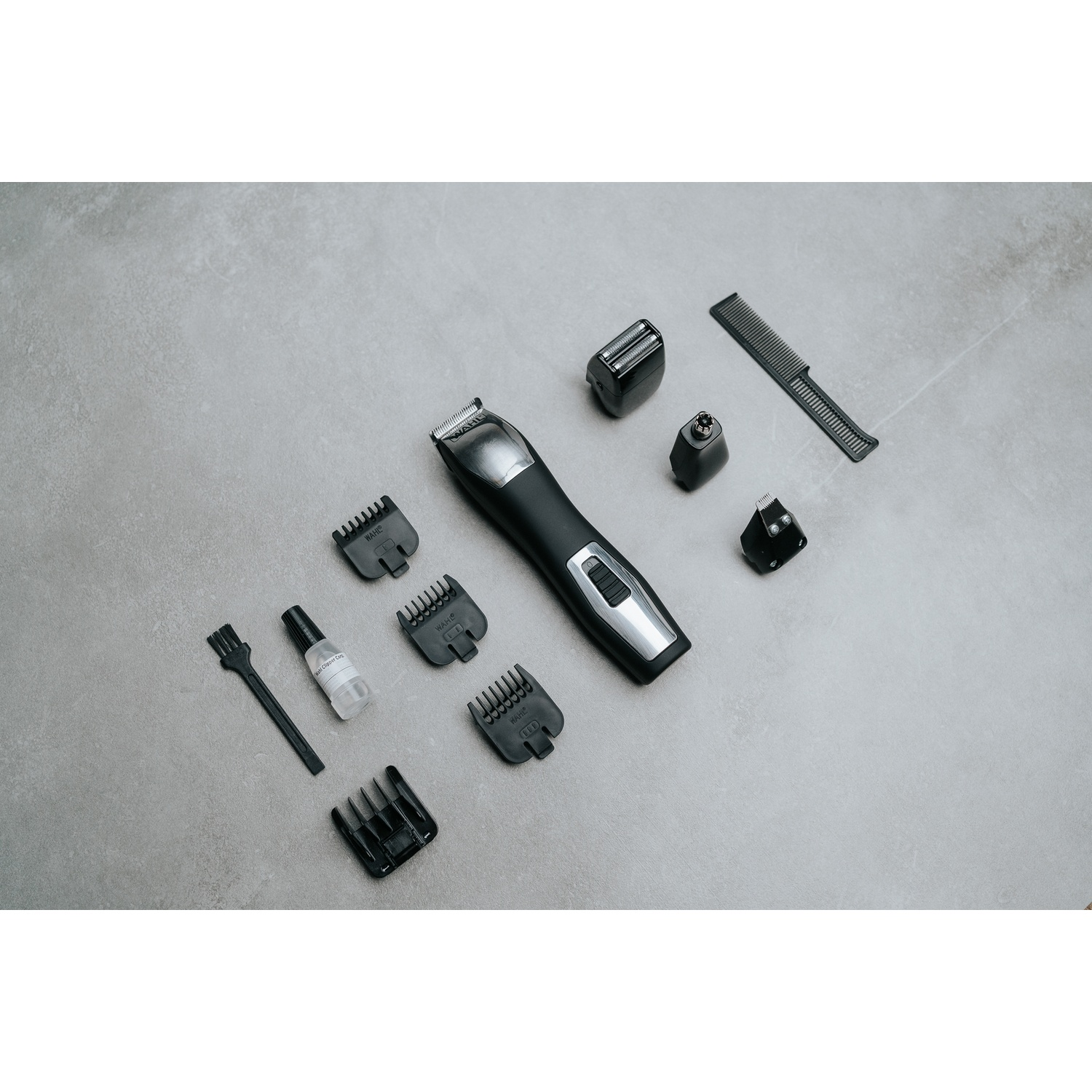 Kit per la toelettatura su una superficie grigia. Include un trimmer, vari accessori, un pettine e una spazzola per la pulizia.