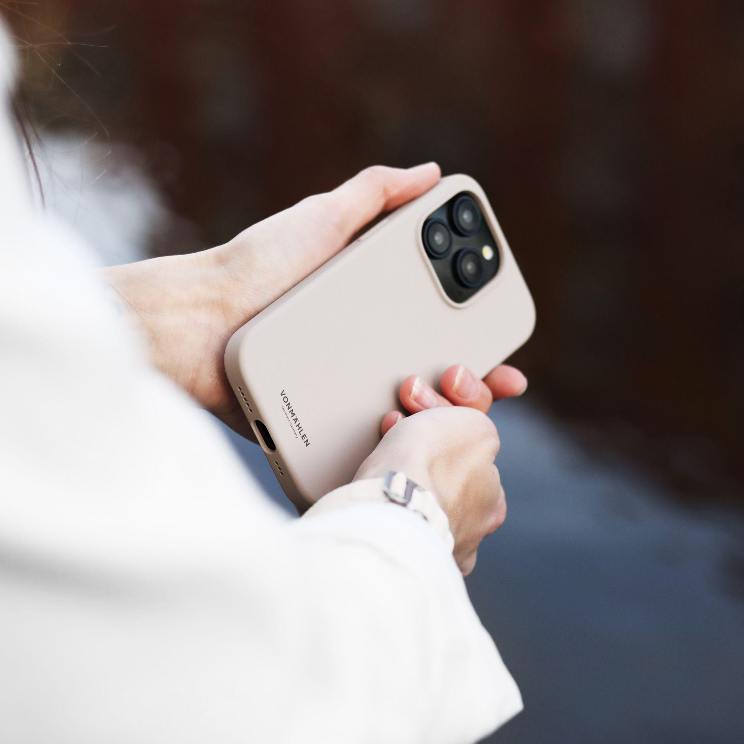 Eine Person hält ein Telefon in einer beigefarbenen Hülle. Der Hintergrund ist unscharf.
