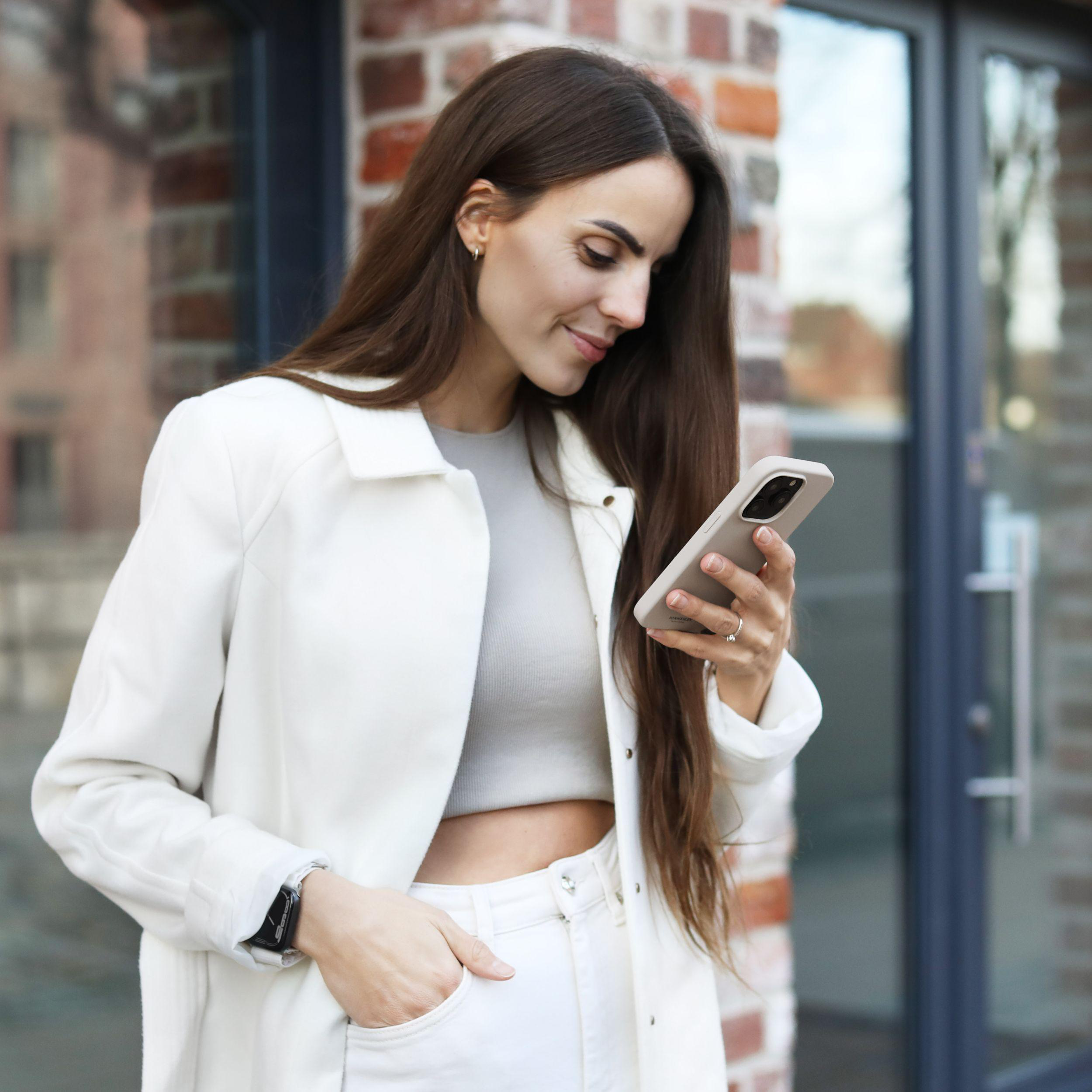 Frau in weißer Jacke, die ein Telefon hält und auf den Bildschirm schaut.