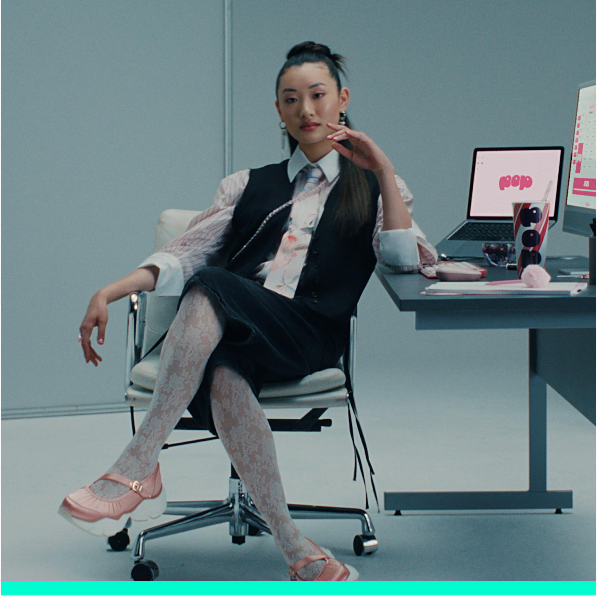 Eine Frau in Business-Outfit sitzt an einem Schreibtisch. Auf dem Schreibtisch liegen ein Laptop und ein Getränk.