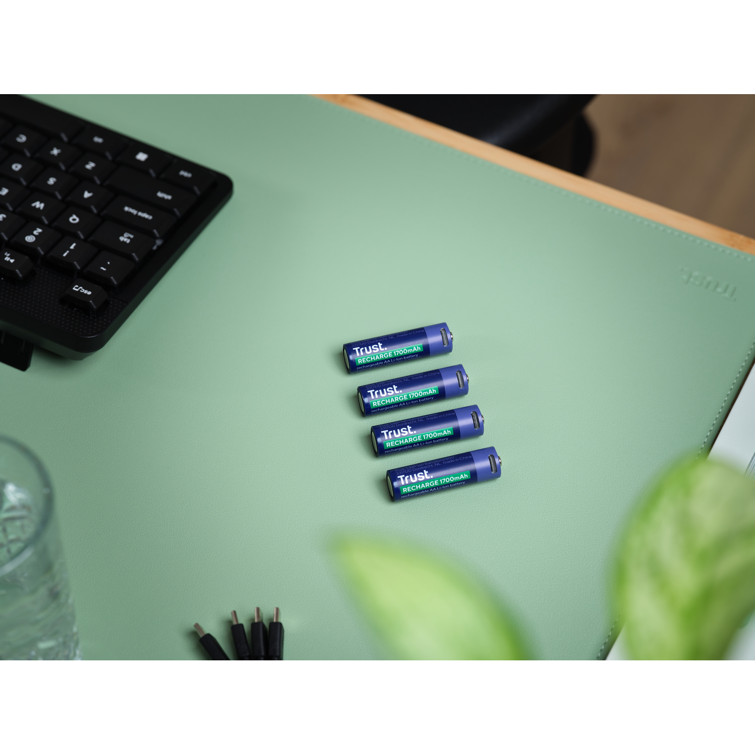 Four blue batteries are arranged on a green desk mat. A black keyboard is visible.