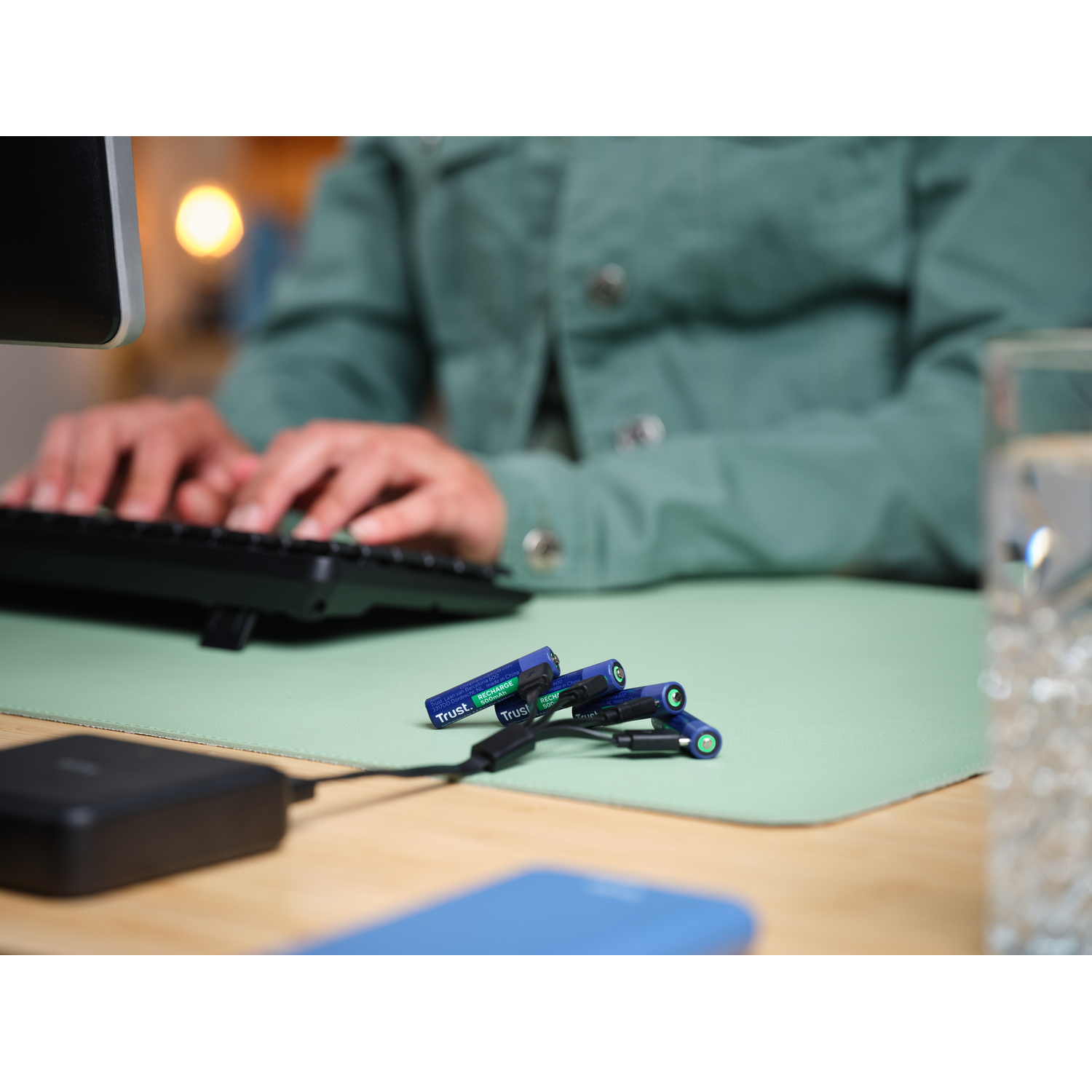 Person typing on keyboard with batteries and charger in the foreground.