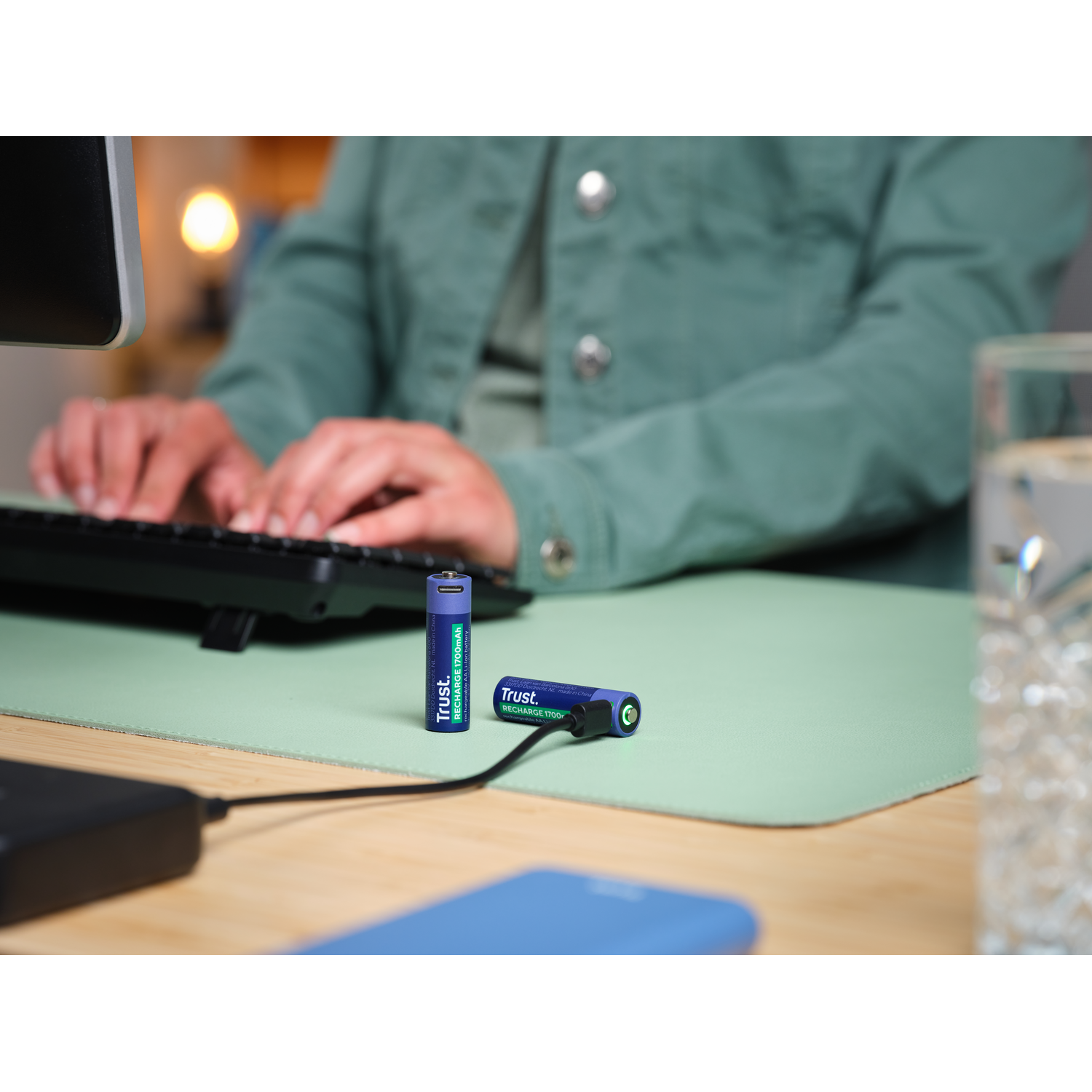 Twee oplaadbare batterijen en een oplaadkabel op een groene bureaumat.