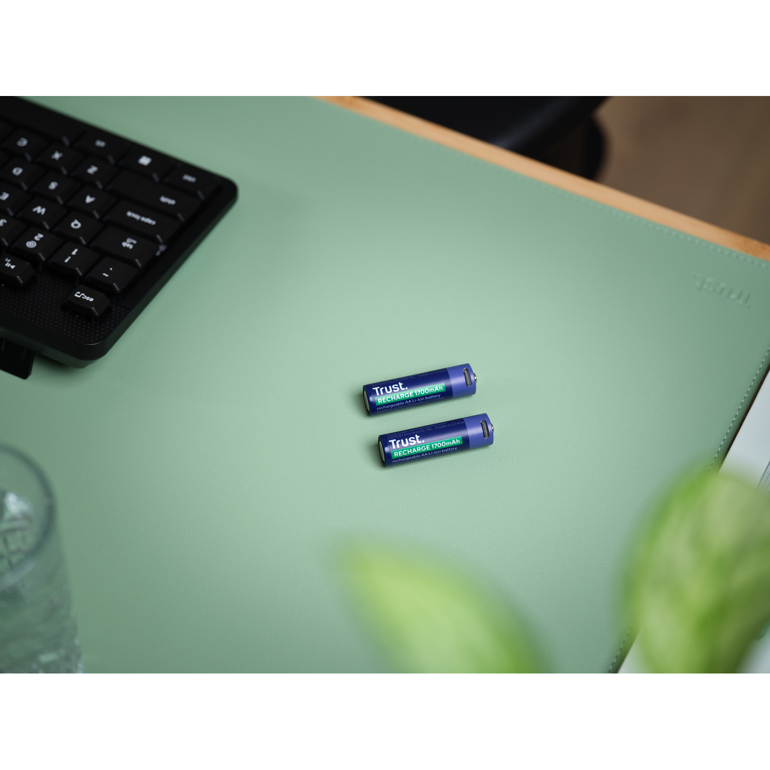 Twee oplaadbare batterijen op een groen bureau, in de buurt van een toetsenbord en een glas.