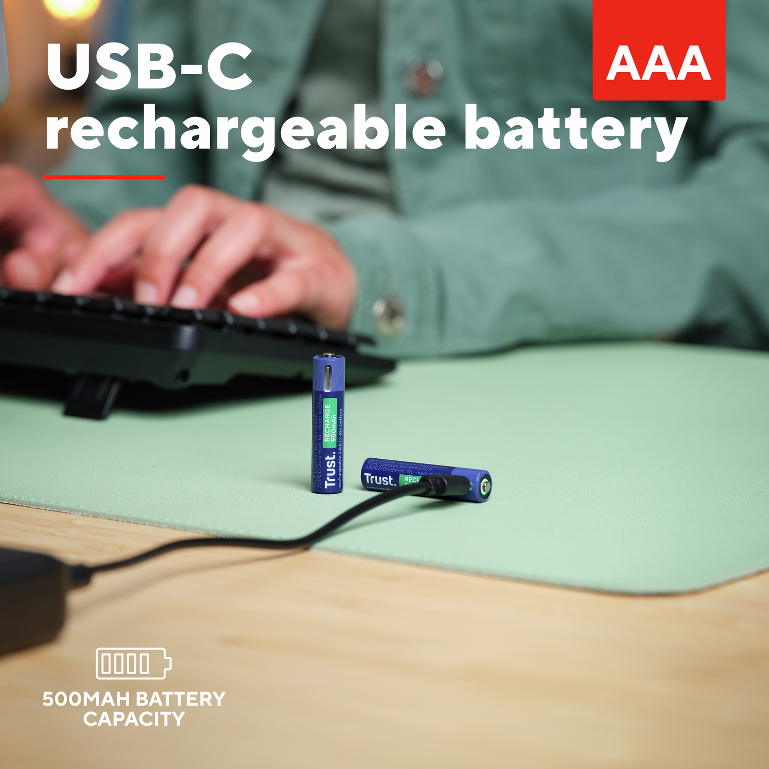 AAA rechargeable batteries, blue, with a USB-C cable, on a green surface. The keyboard and hands are visible.