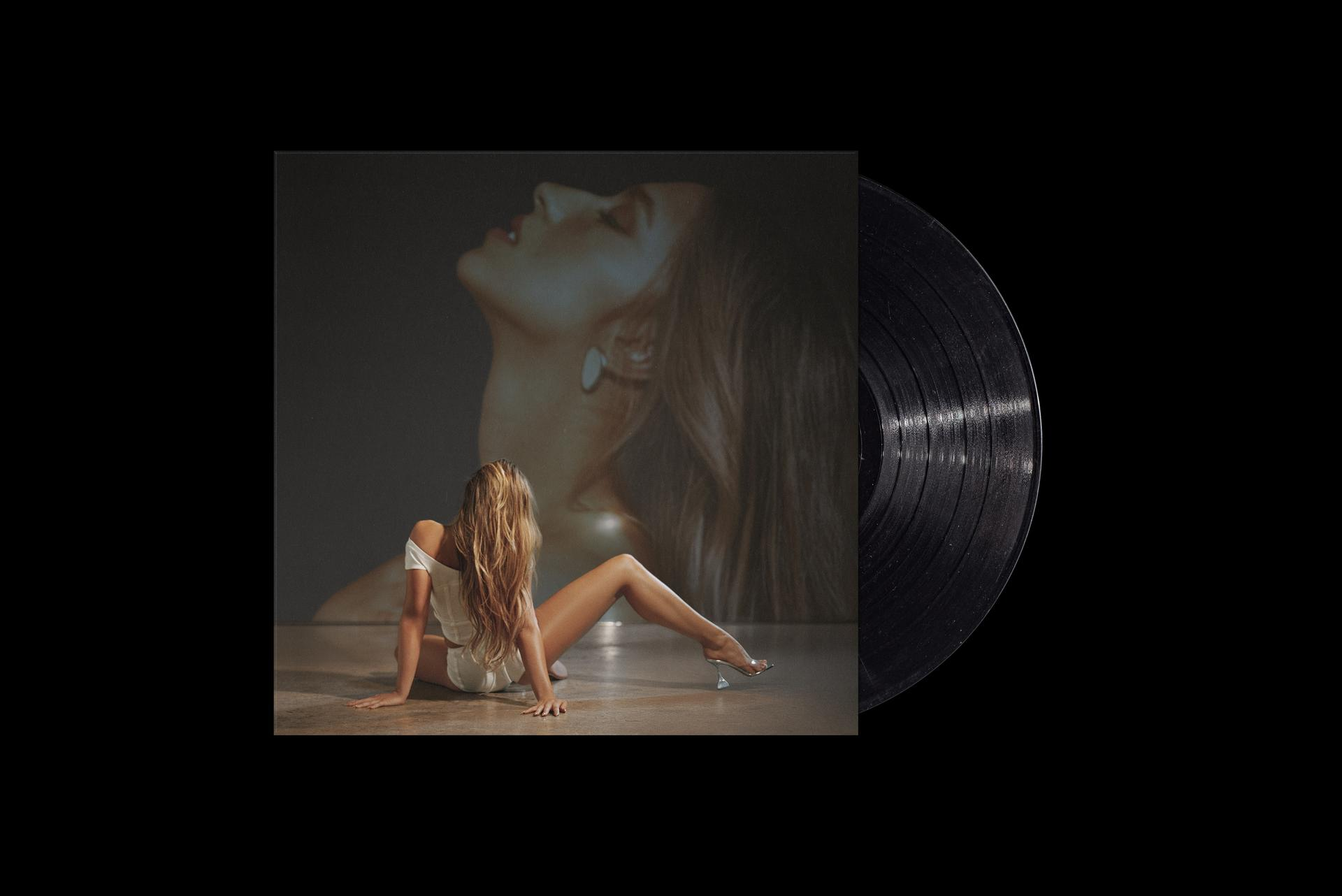 Vrouw zittend op de grond met een vinylplaat. Een foto staat op de achtergrond.
