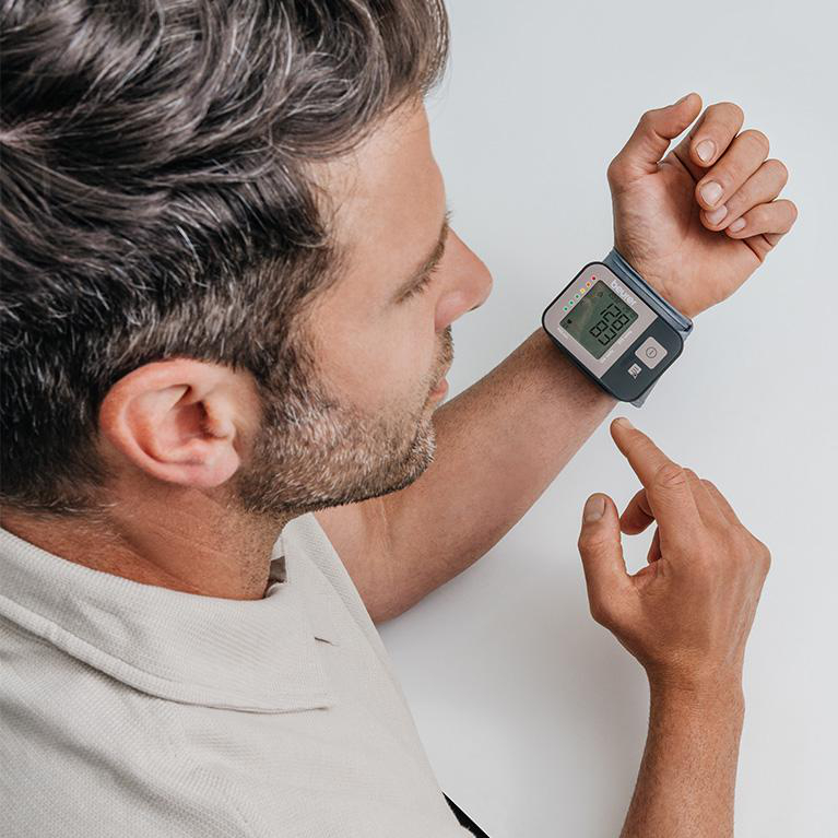 Mann trägt Smartwatch, überprüft das Display. Er zeigt mit der anderen Hand darauf.