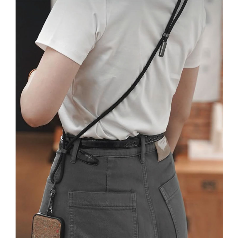 Mujer de espaldas, con camisa blanca y pantalón gris, lleva una funda de teléfono con correa.