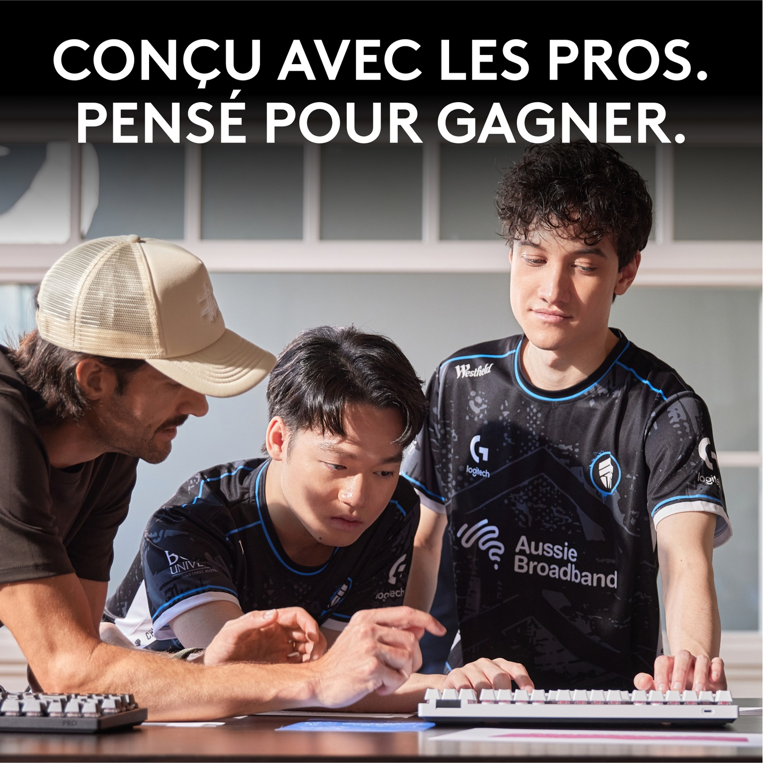 Trois jeunes hommes regardent un clavier. L'un porte une casquette et une barbe ; les autres des maillots de gaming.