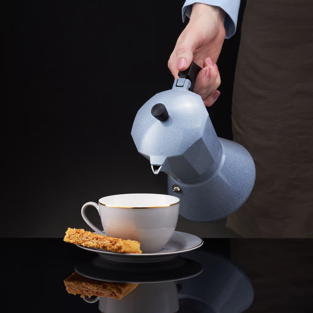 Osoba nalewająca kawę z niebieskiego, nakrapianego ekspresu do kawy do filiżanki z ciasteczkiem.