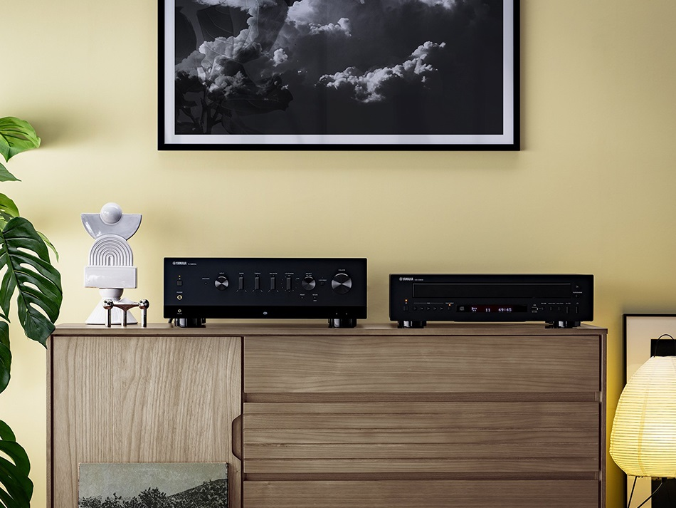 System stereo na drewnianej szafce. Sprzęt stereo i lampa przed żółtą ścianą.