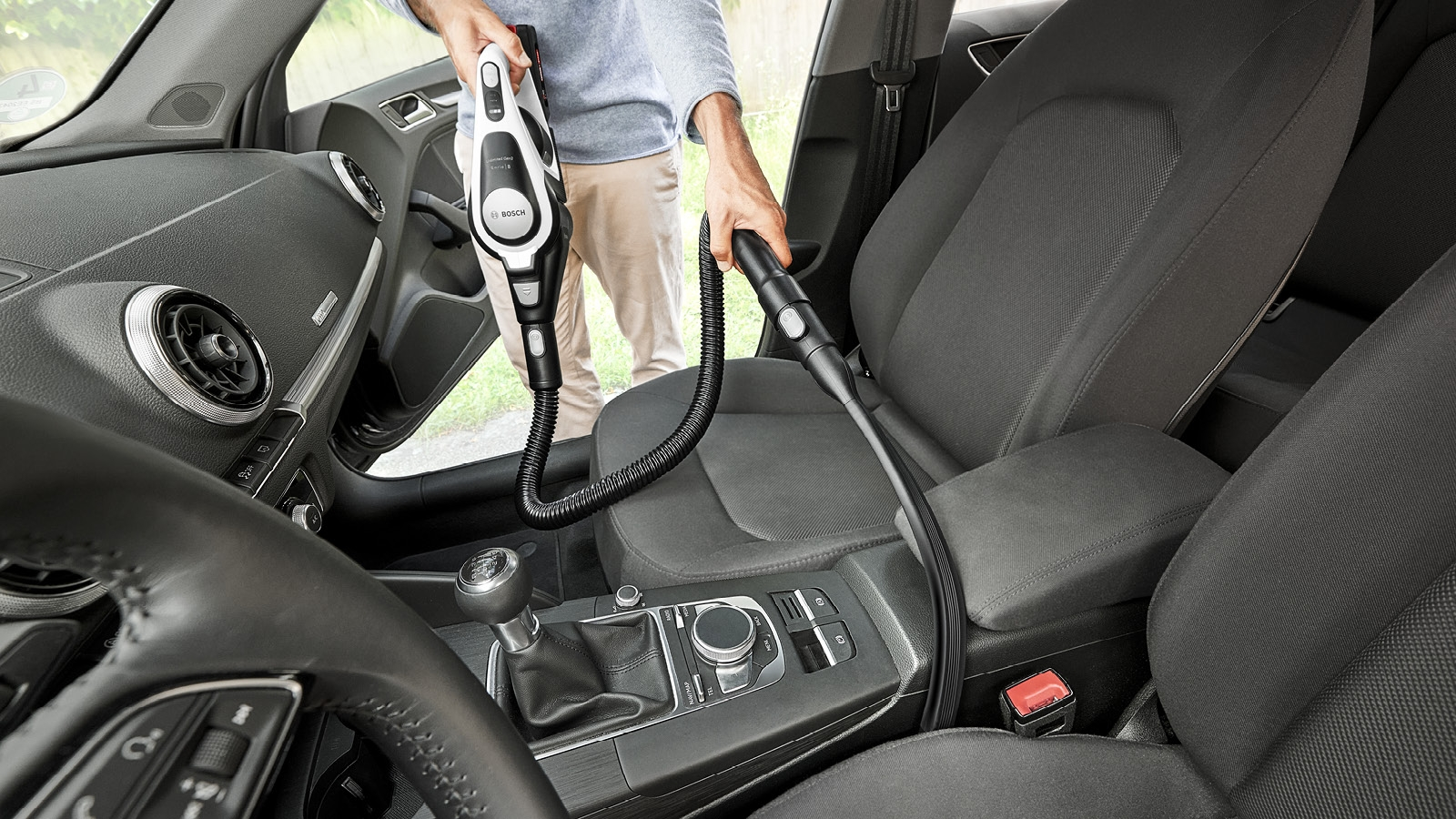 Eine Person, die den Innenraum eines Autos mit einem Bosch-Staubsauger absaugt. Das Auto hat schwarze Sitze und ein Armaturenbrett.