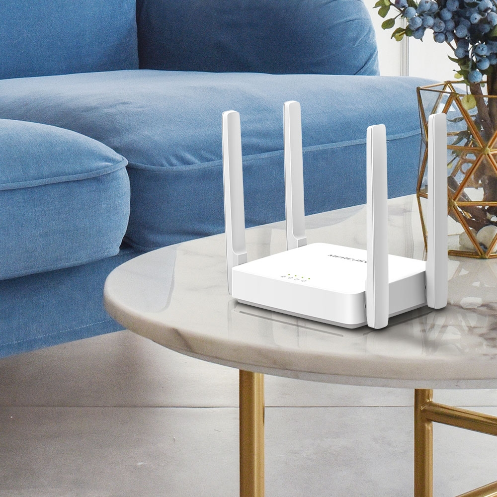 Biały router z czterema antenami stoi na marmurowym stole. W tle niebieska sofa i wazon z kwiatami.