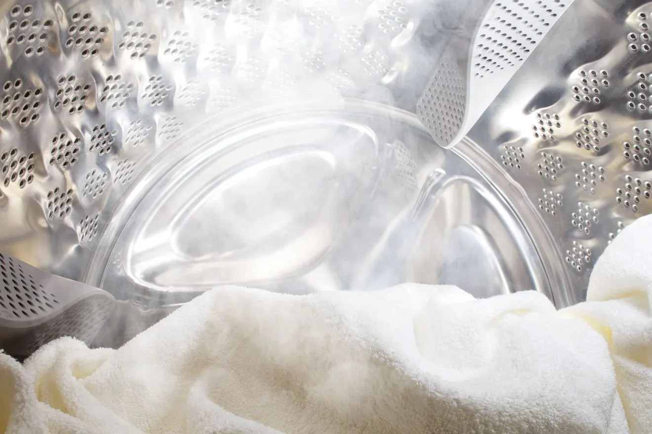 Wnętrze bębna pralki z białym ręcznikiem i parą.