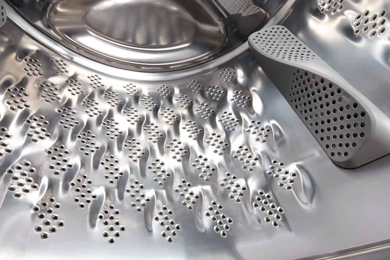 Wnętrze błyszczącego, stalowego bębna pralki z wieloma otworami.