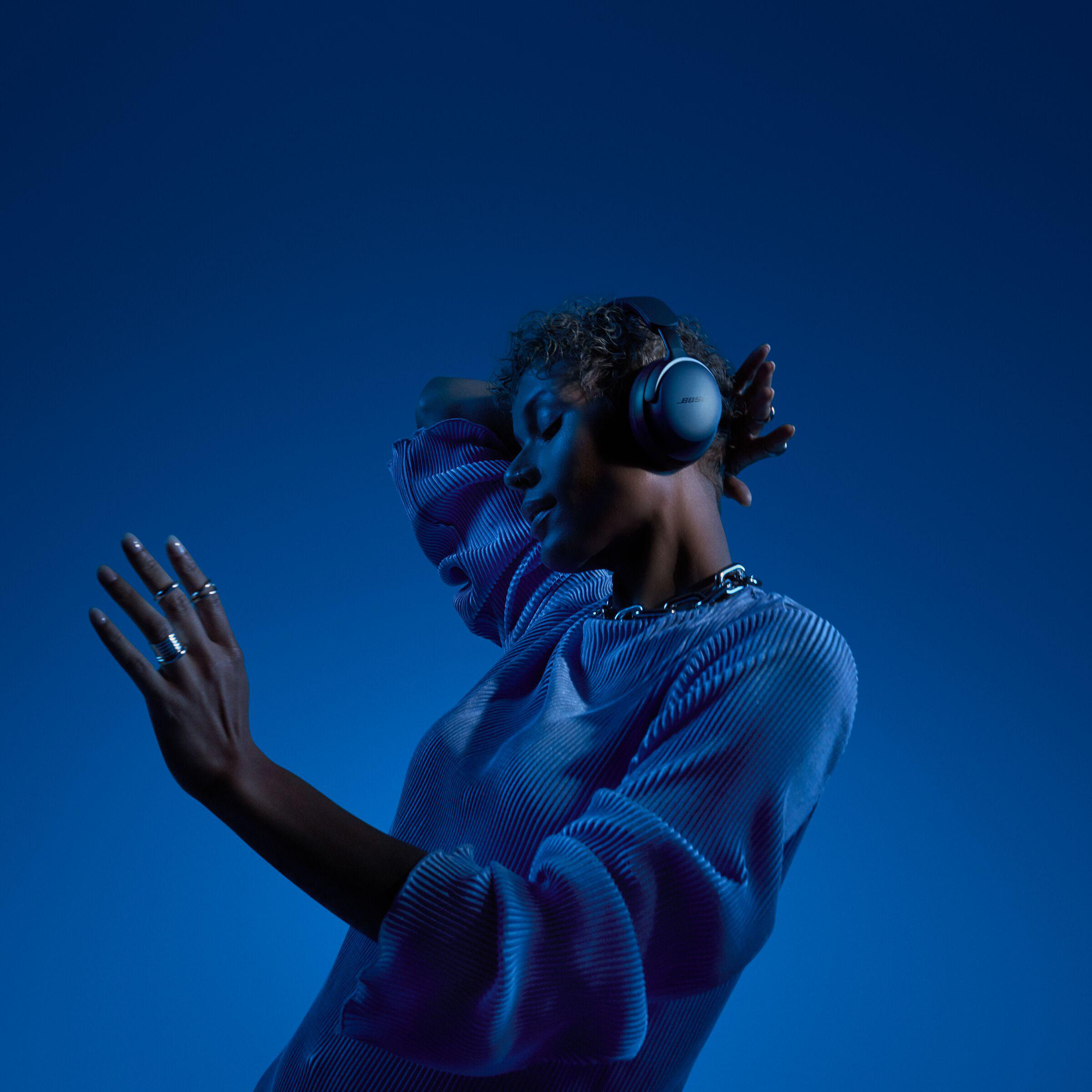 Frau mit Kopfhörern, posiert mit hochgelegten Armen, blauer Hintergrund.