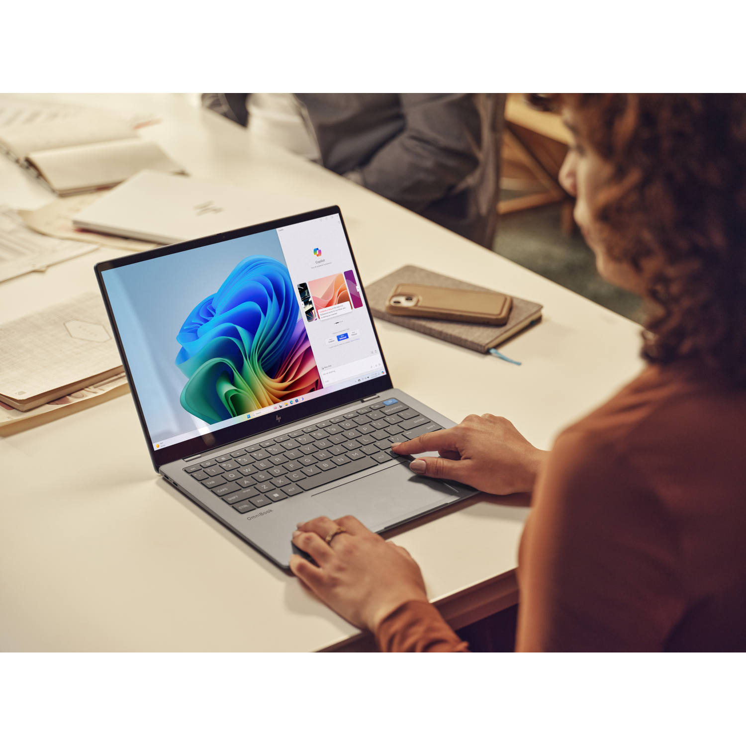 Femme utilisant un ordinateur portable sur un bureau avec un carnet et un téléphone.