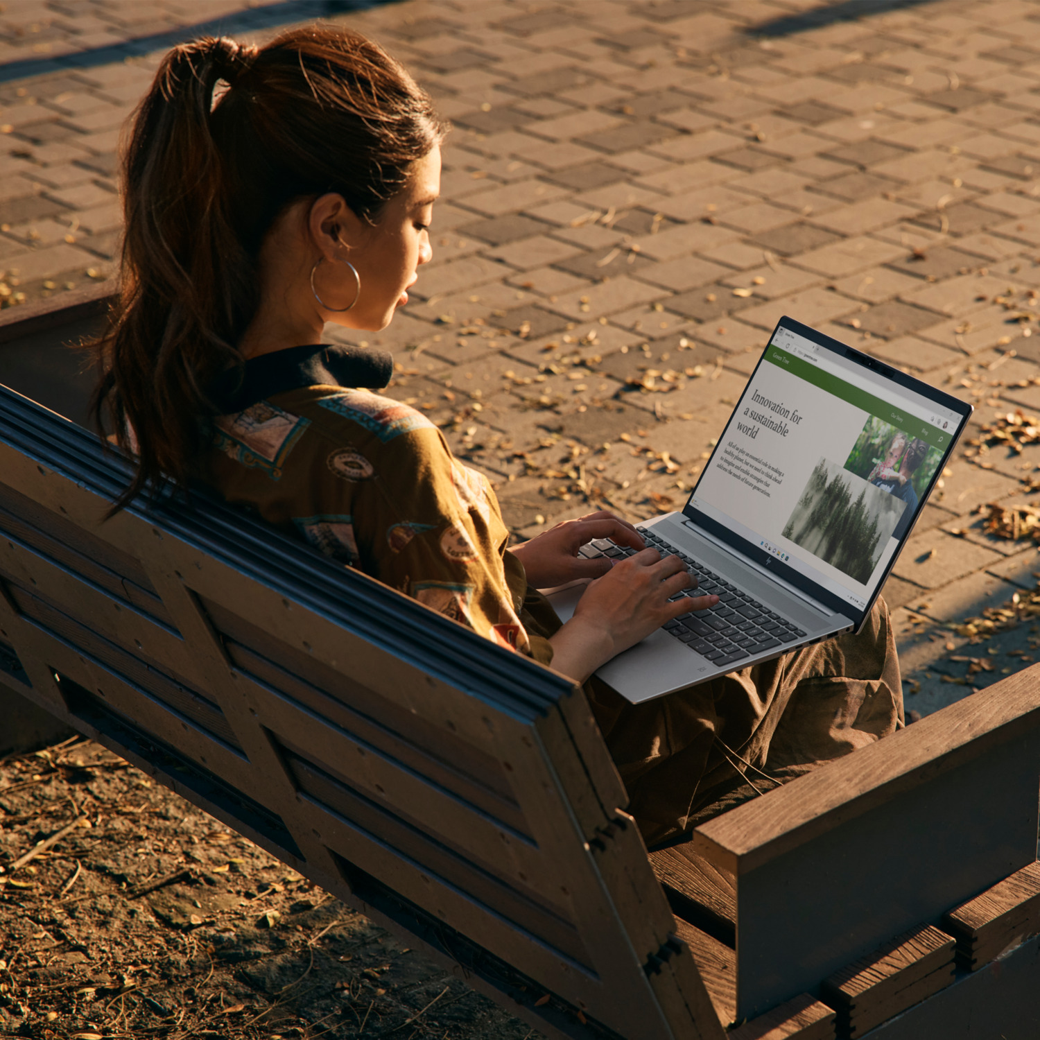 Vrouw werkt buiten op een laptop, zittend op een bank. Het scherm toont tekst en afbeeldingen.