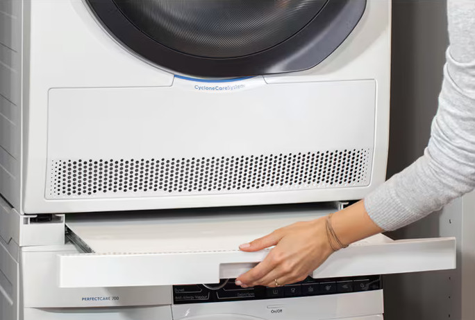 Dłoń kobiety wyciąga białą szufladę z białego zestawu pralki i suszarki.