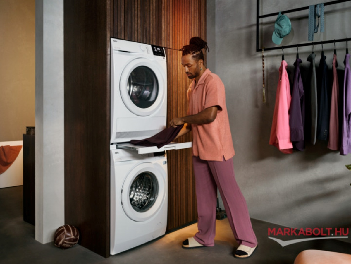 Mężczyzna wyjmuje ubrania z suszarki obok pralki.