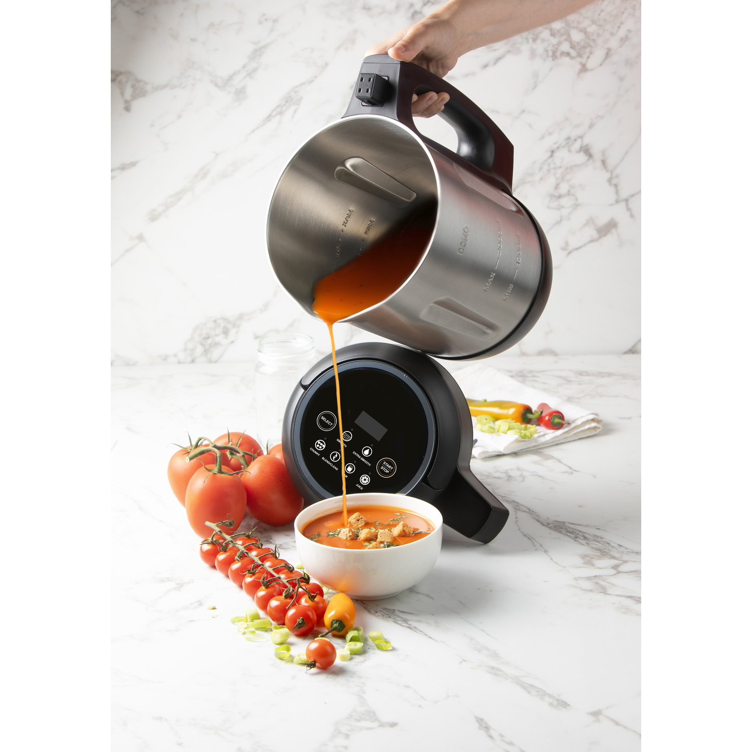 Soup is being poured from a stainless steel pot into a bowl with ingredients around it. Tomato soup.