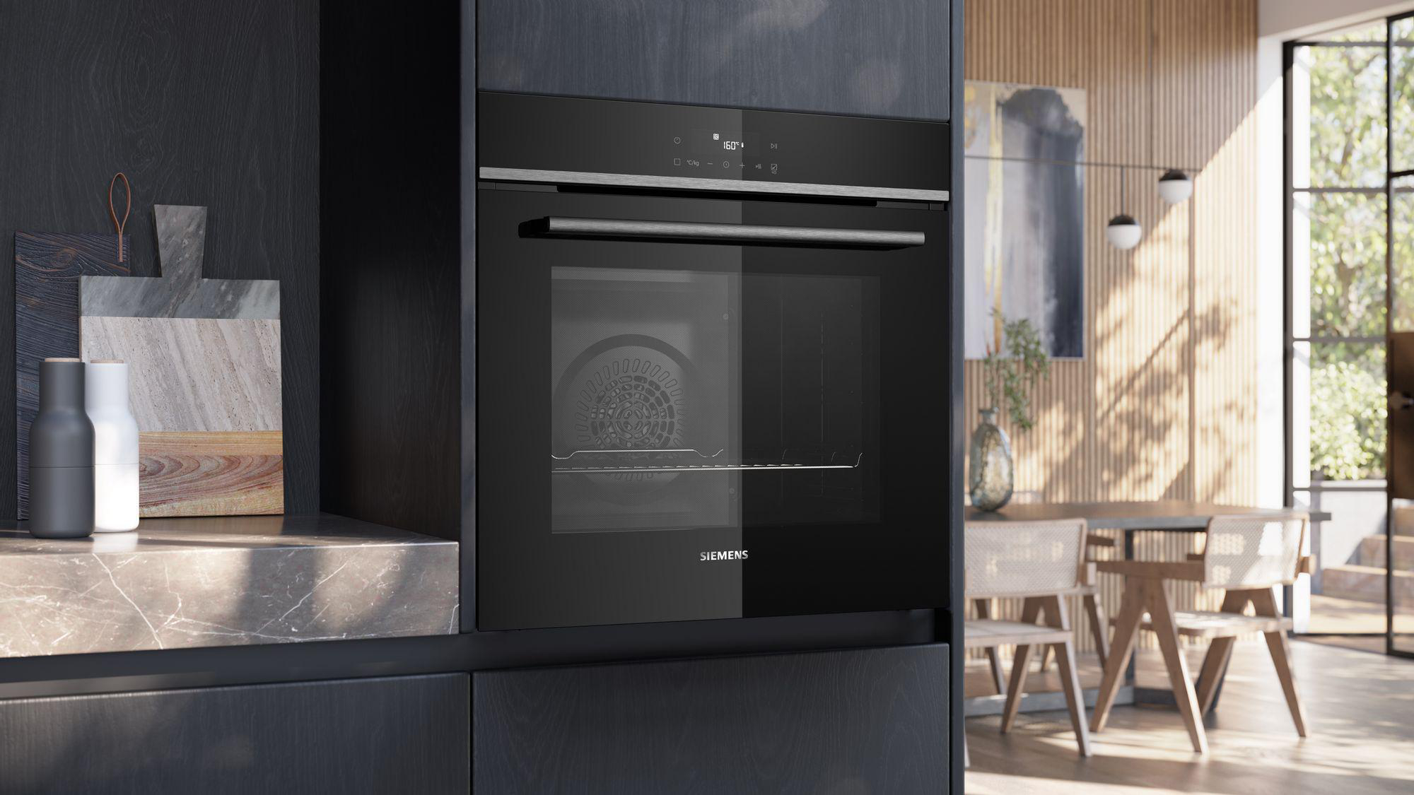 Ein schwarzer Siemens-Backofen ist in eine dunkle Küche mit Holztisch und Stühlen eingebaut.