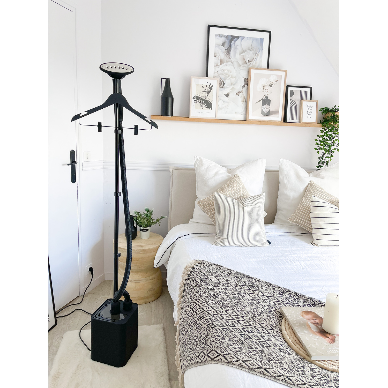 A bedroom with a clothes steamer, art, and a bed. White walls and a rug are also visible.