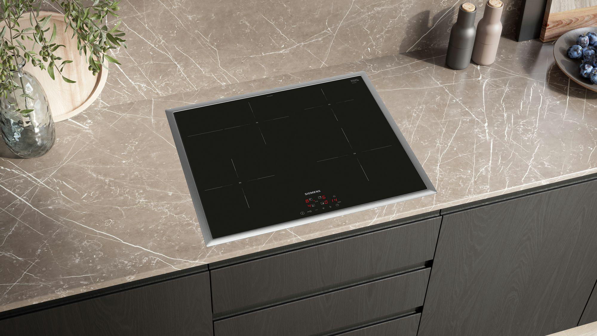 Schwarzes Induktionskochfeld mit silberner Leiste auf Marmor-Arbeitsplatte, über dunklen Schränken.